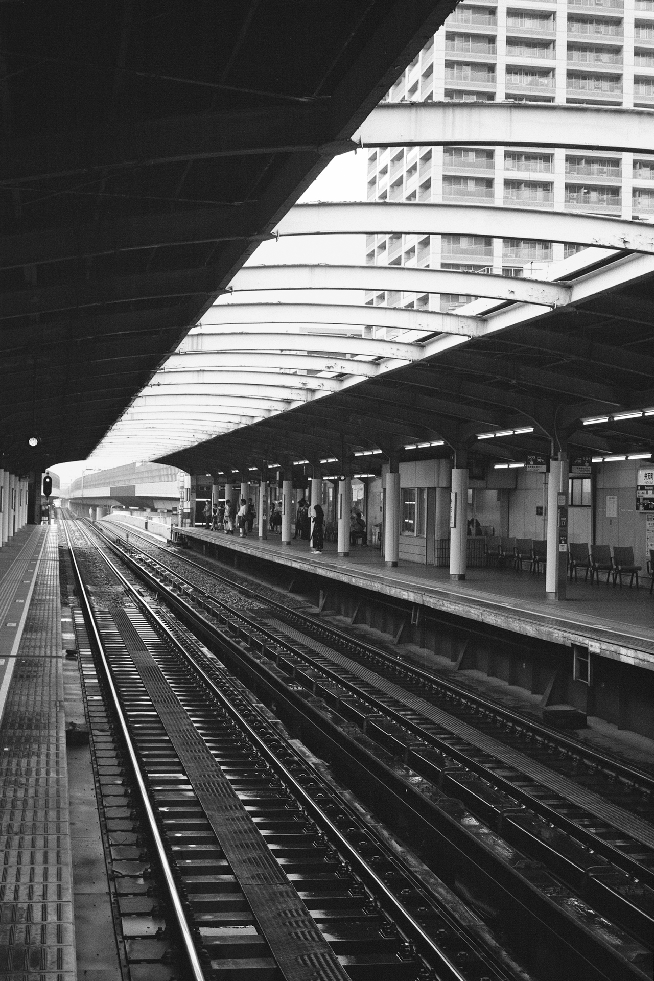 Black and white Bentencho station platform lone person sitting on chair fluorescent lighting Japanese signage