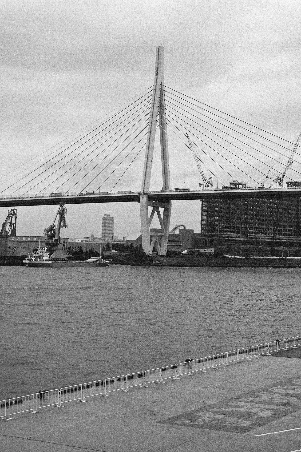 Black and white cable-stayed bridge over harbor with boats and industrial port area