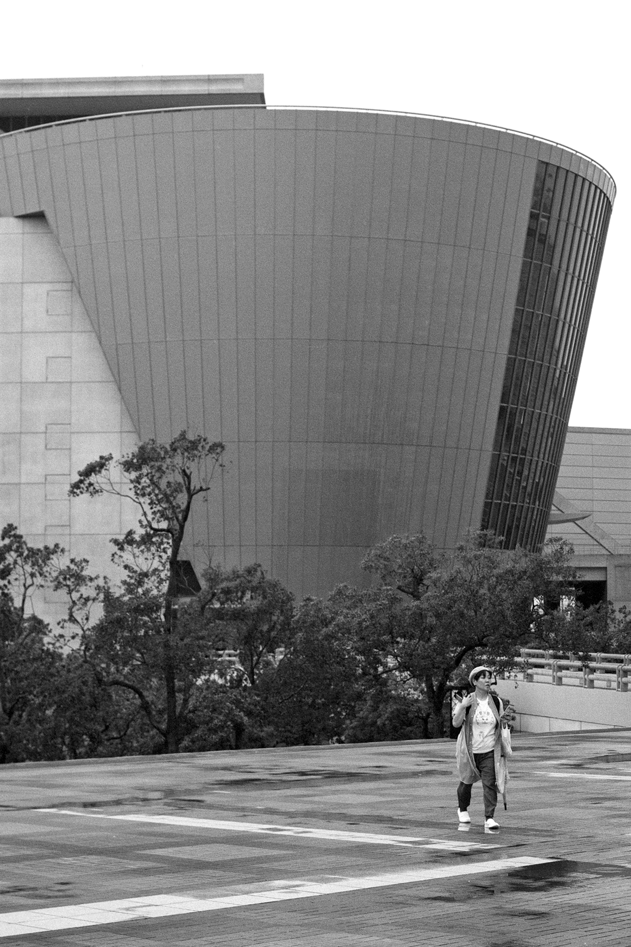 Black and white person walking near massive curved modern architecture Osaka Aquarium area