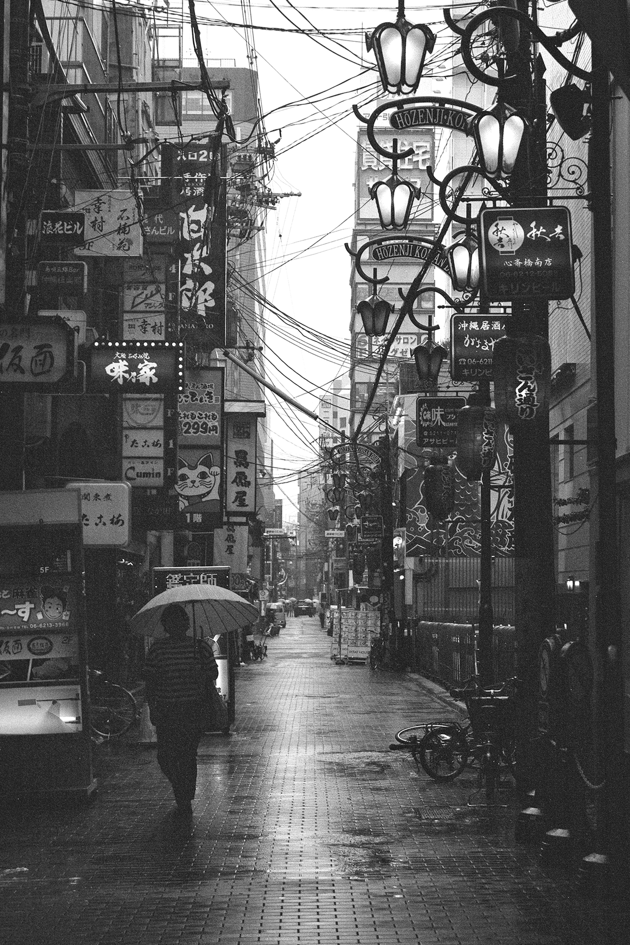 Black and white rainy narrow Osaka alley Hozenji Yokocho with neon signs lanterns person umbrella