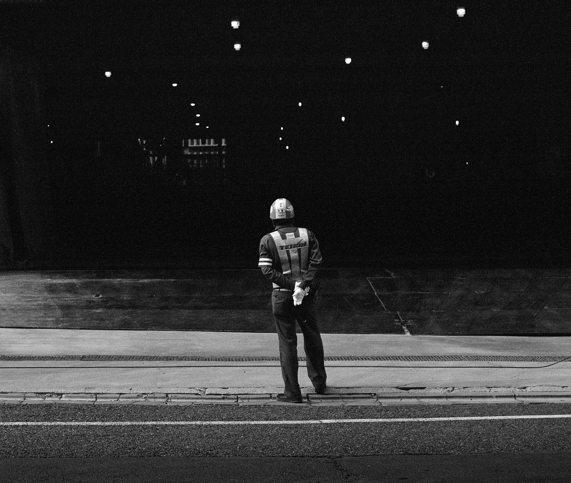 Black and white night scene worker in reflective vest standing by construction site distant lights