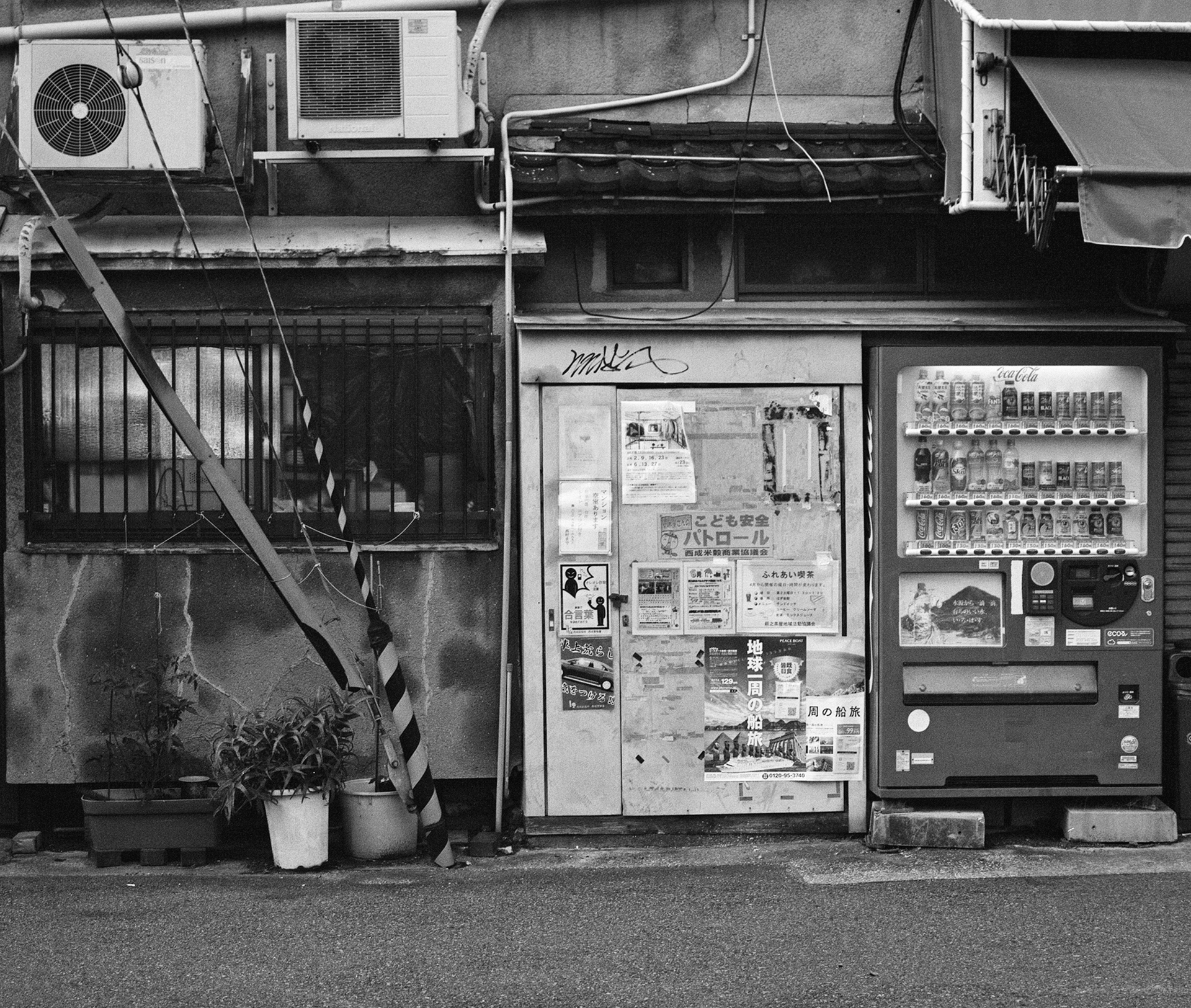 Black and white street scene weathered building facade vending machine posters air conditioning units
