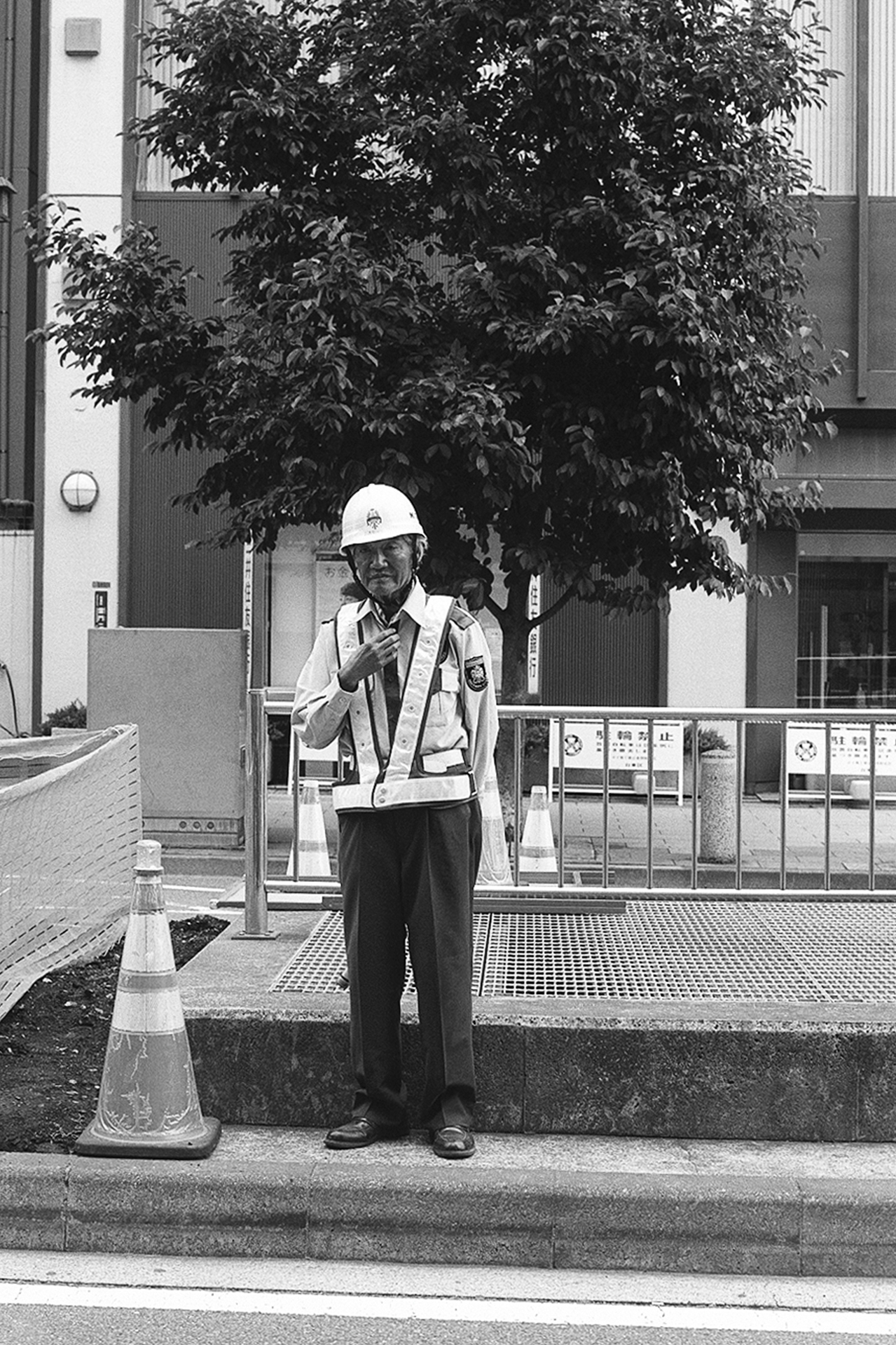 Black and white construction traffic controller in hard hat safety vest at work site with cone