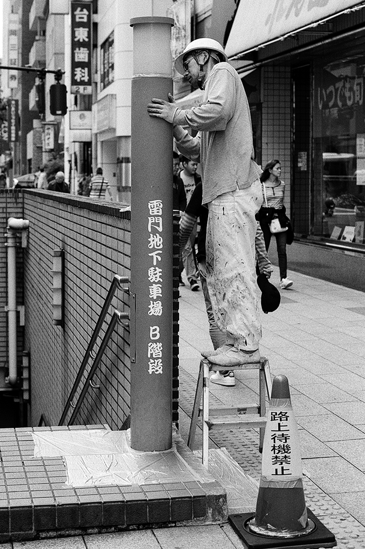 Black and white painter worker on ladder painting lamp post Kaminarimon underground parking stairs