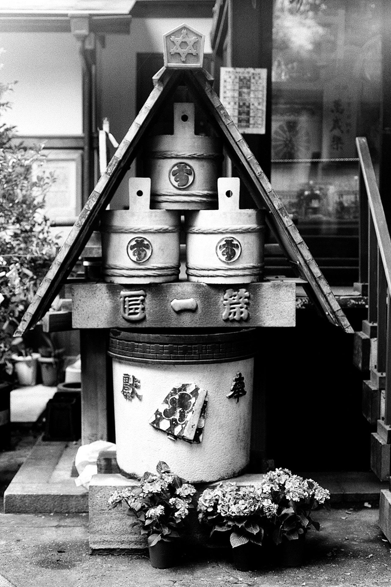 Black and white traditional sake barrels stacked in triangular wooden frame display with hydrangea flowers