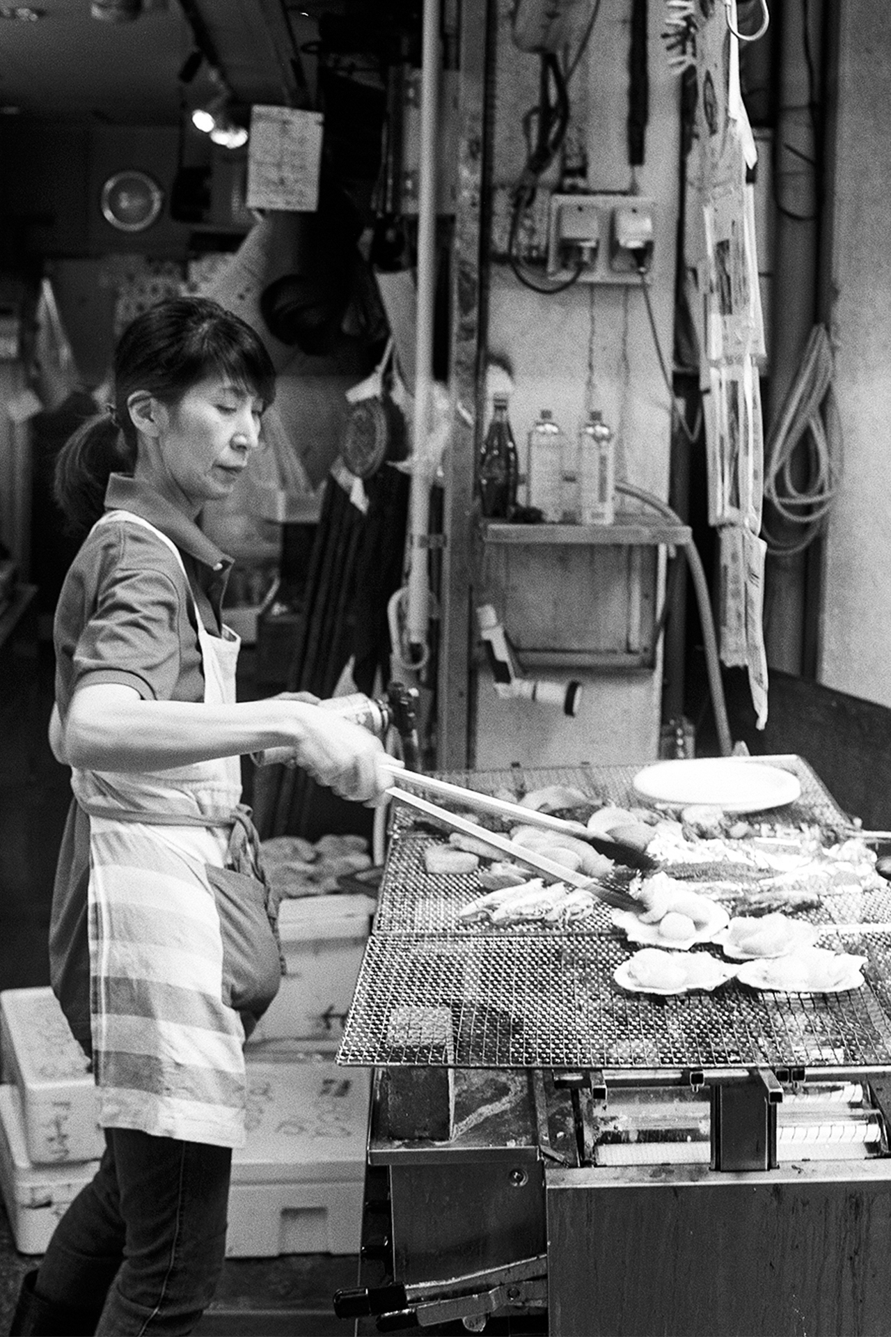 Black and white woman in apron grilling seafood scallops fish on charcoal grill market stall