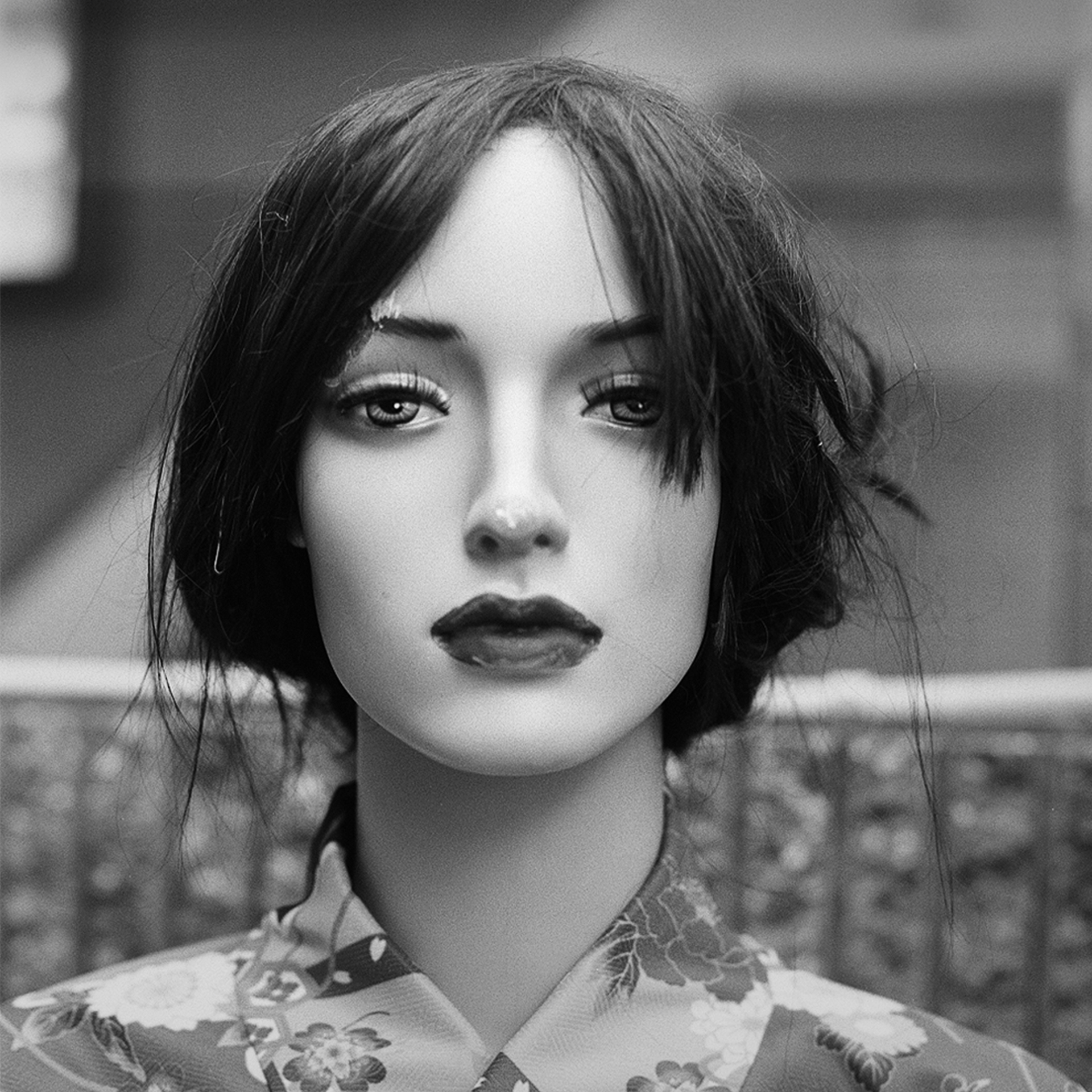 Black and white close-up portrait of mannequin with realistic features dark hair floral patterned shirt