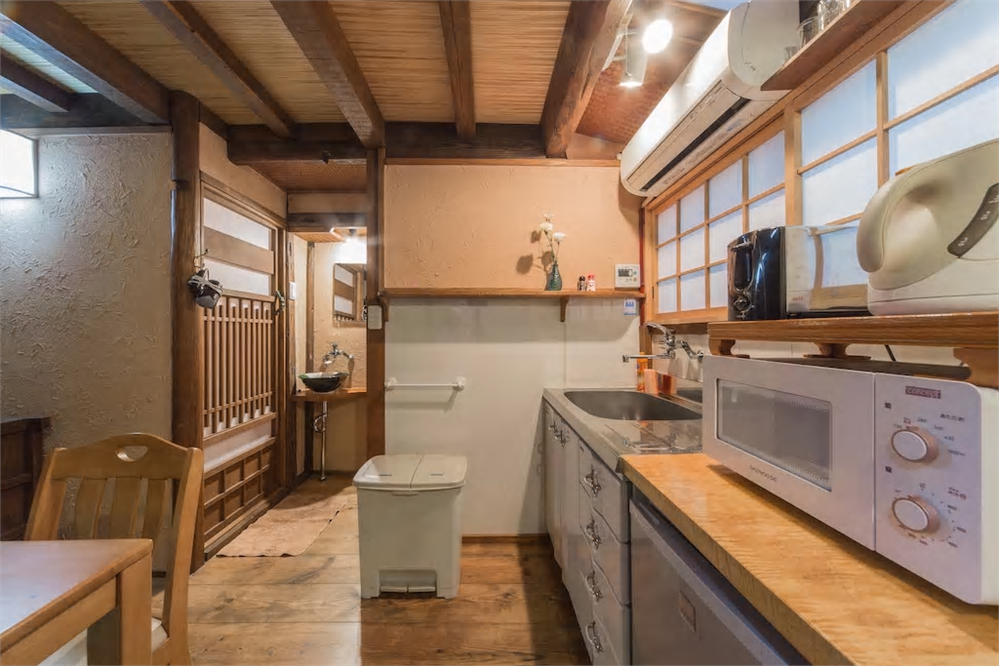 Rustic machiya kitchen with stainless counters, microwave, traditional wooden lattice partition, ceramic vessel sink, and exposed beams