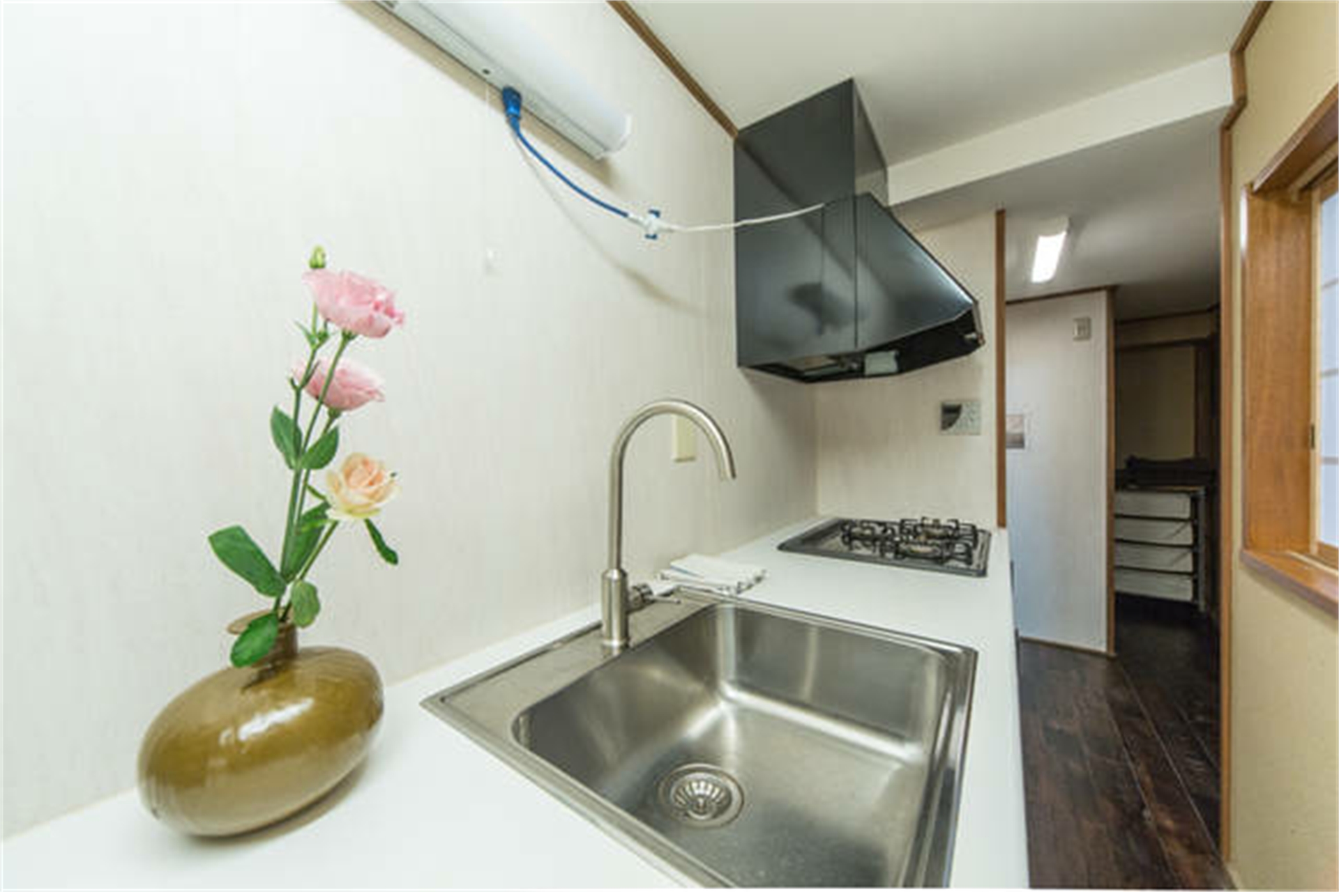 Modern white kitchen with stainless steel sink, gas cooktop, black range hood, and decorative vase with pink roses