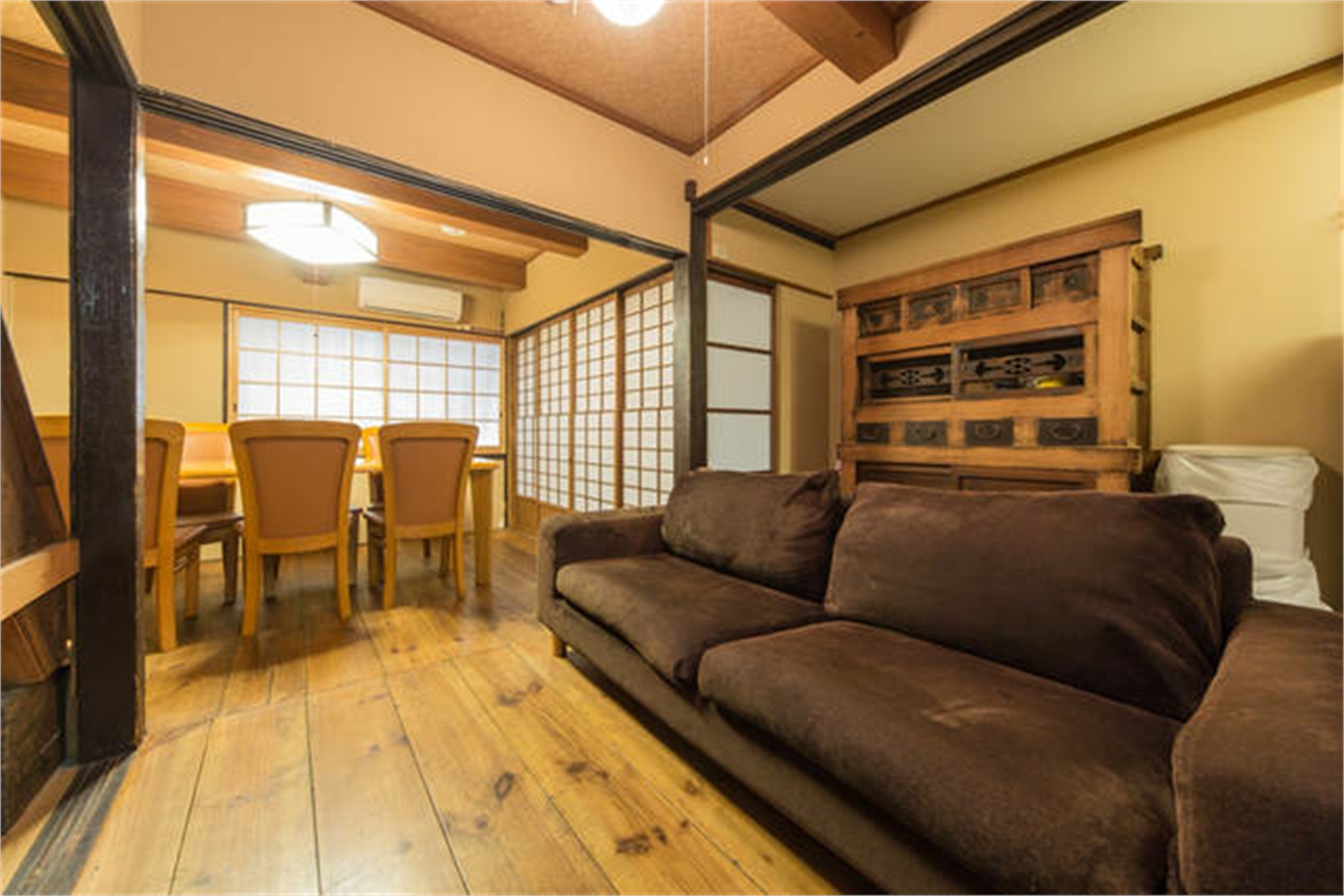 Juichi-An living room with brown velvet sofa, antique tansu cabinet, wooden plank floors, dining area with shoji screens, and exposed ceiling beams