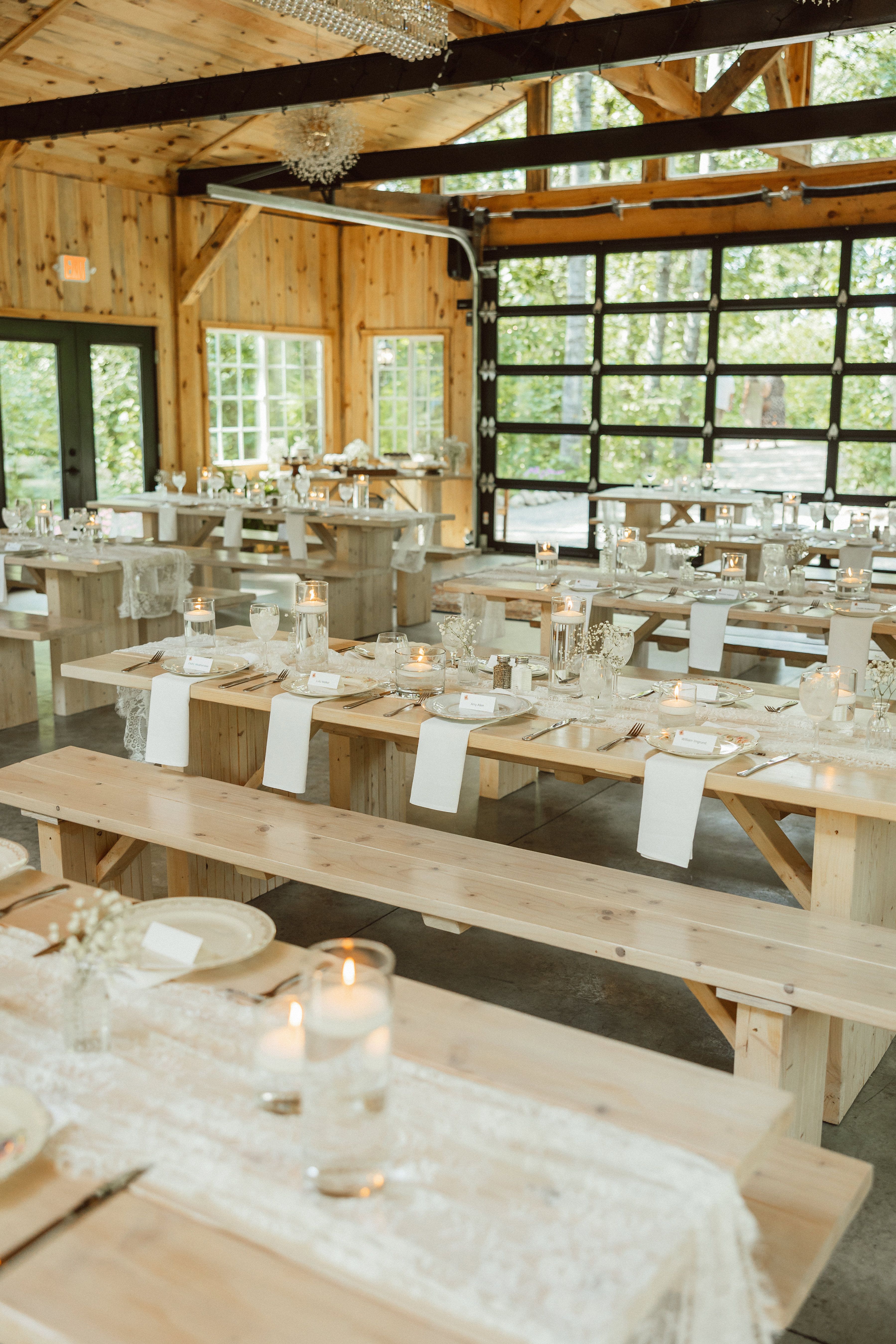 A candlelit wedding reception inside The Emerald Cottage with long tables, chandeliers, and woodland views