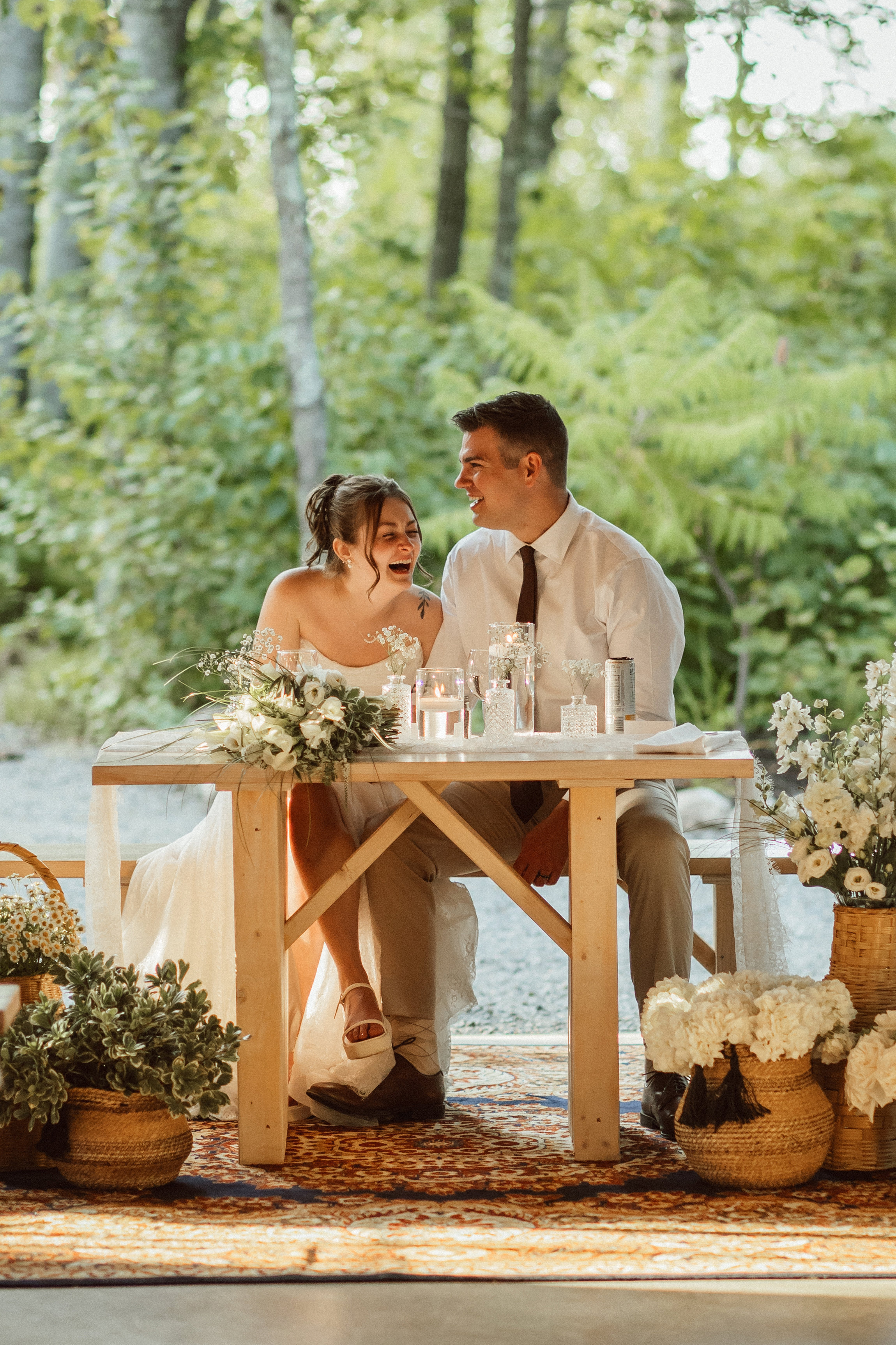 A couple laughing together at their reception table surrounded by flowers and candlelight