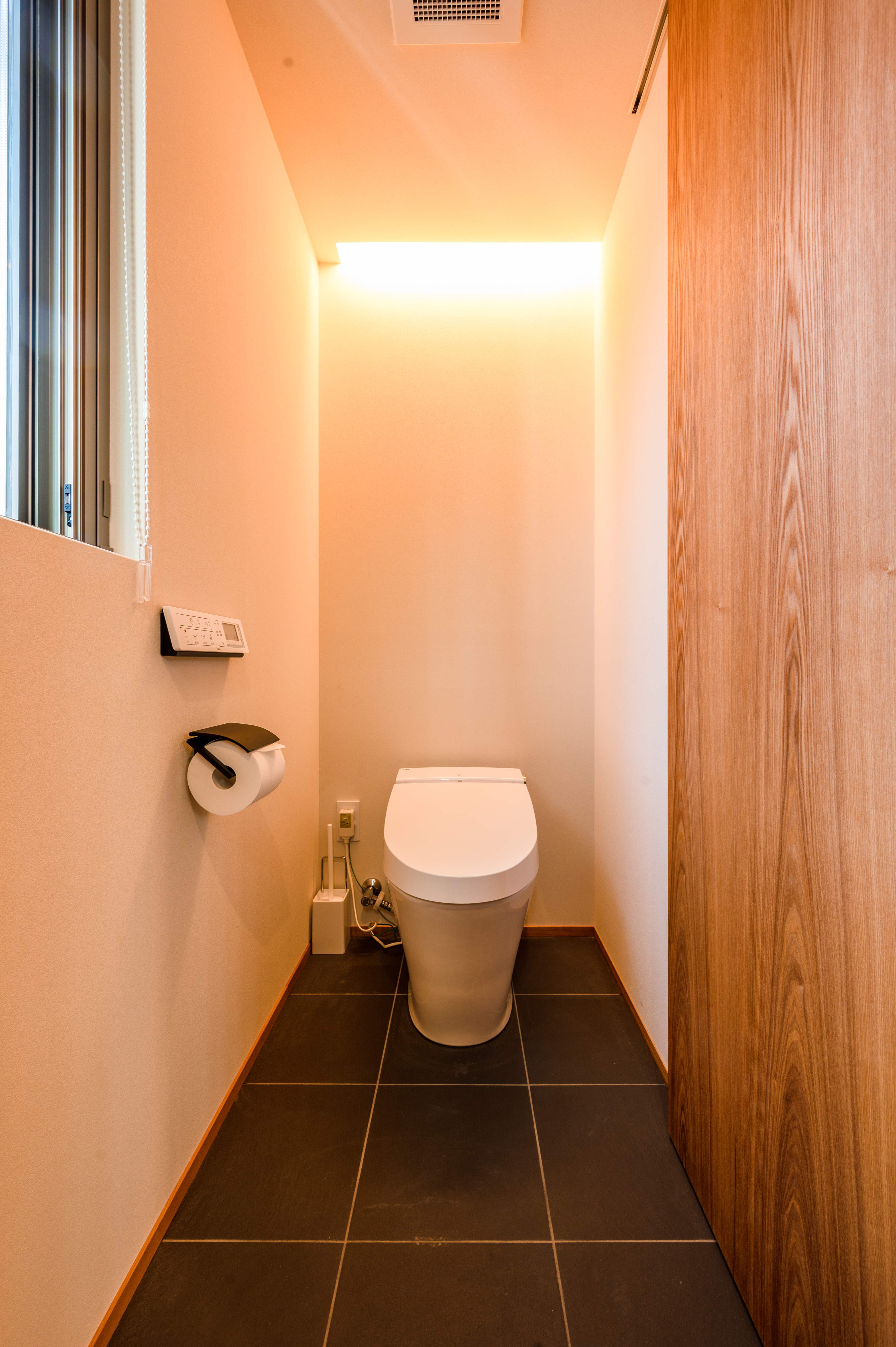 Modern separate toilet room with warm peachy walls, dark slate floor, and high-tech Japanese toilet