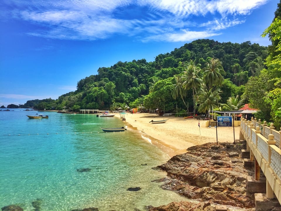 Kapas Island beach with turquoise water, fishing boats, palm trees and rainforest hillside, Terengganu Malaysia
