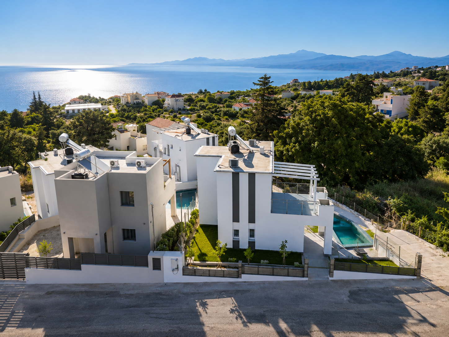 Aerial view of modern white villas in Crete with swimming pools and panoramic sea view