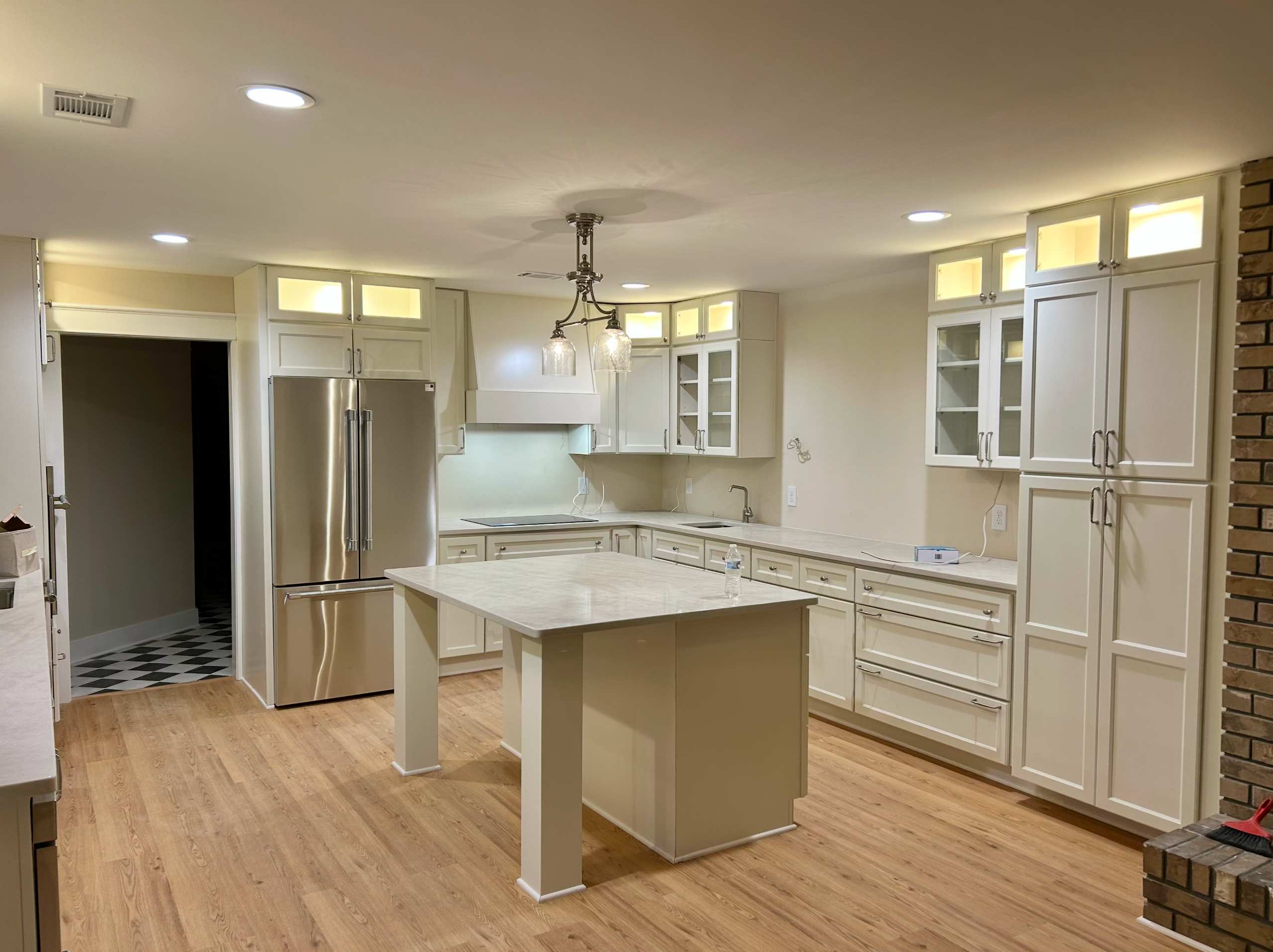 Renovated kitchen with cream cabinetry, a marble-top island, stainless refrigerator, and glass-front upper cabinets over wood floors