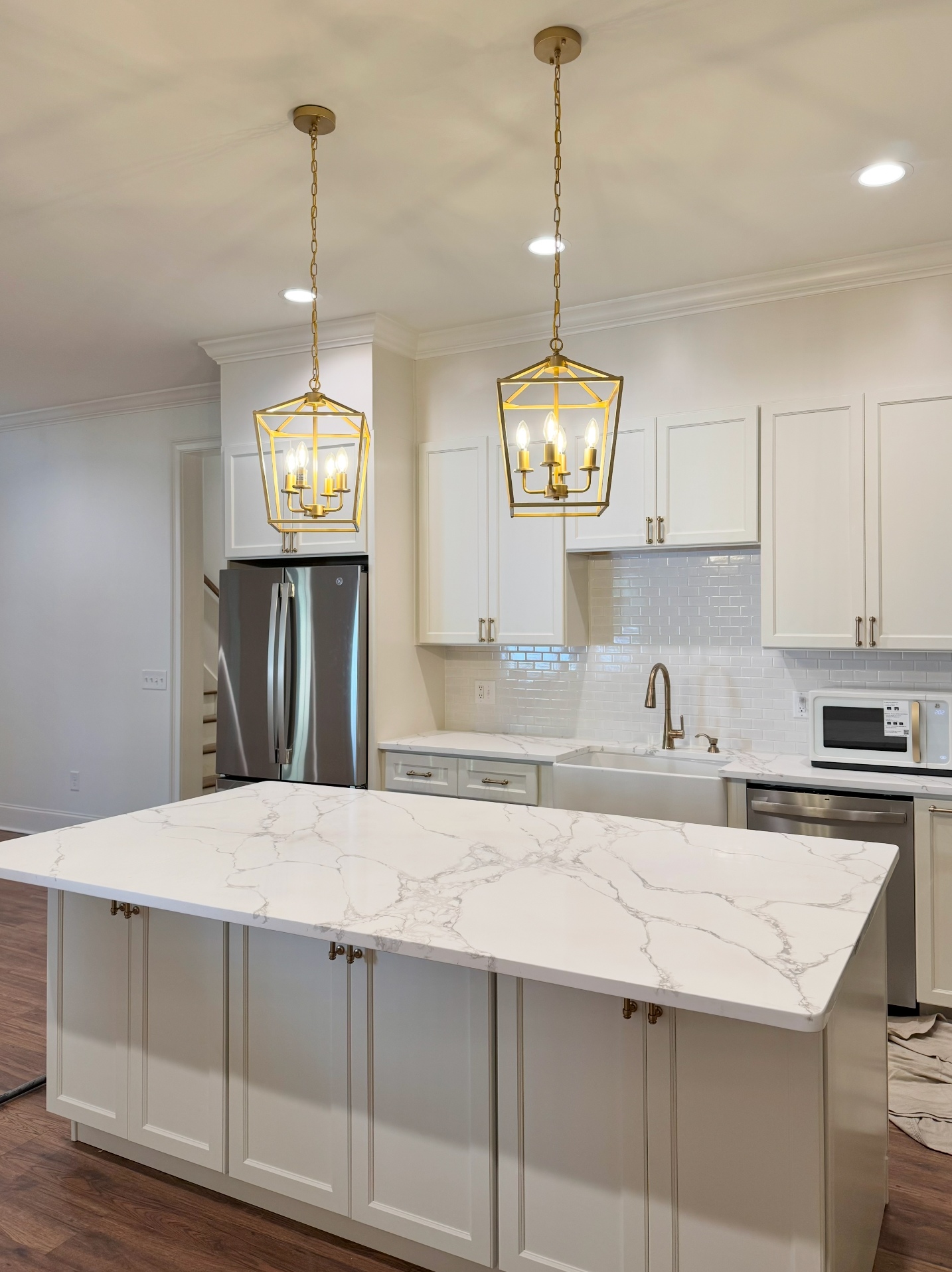Remodeled kitchen with a large white-marble waterfall island, twin gold lantern pendants, a farmhouse sink, and white shaker cabinetry