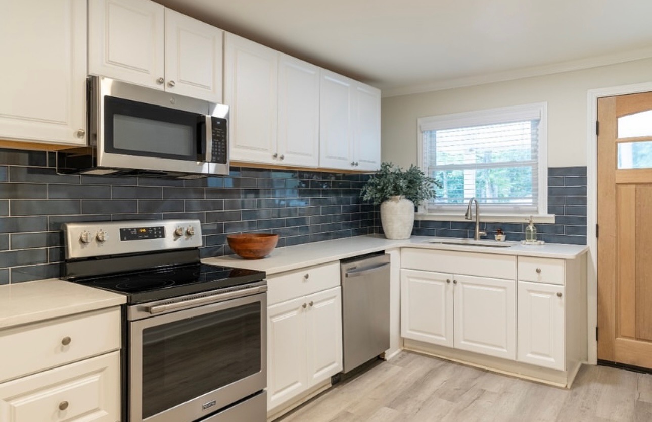 Bright kitchen with a navy subway-tile backsplash, white cabinets, stainless appliances, and a wood entry door