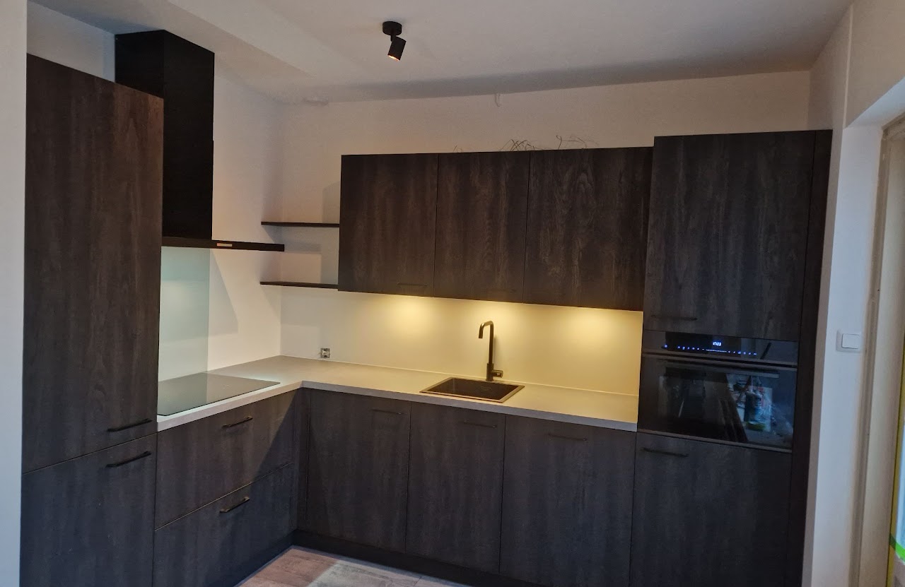 Keuken met donkere houtlook kasten, licht werkblad, zwarte kraan en verlichting onder de bovenkasten