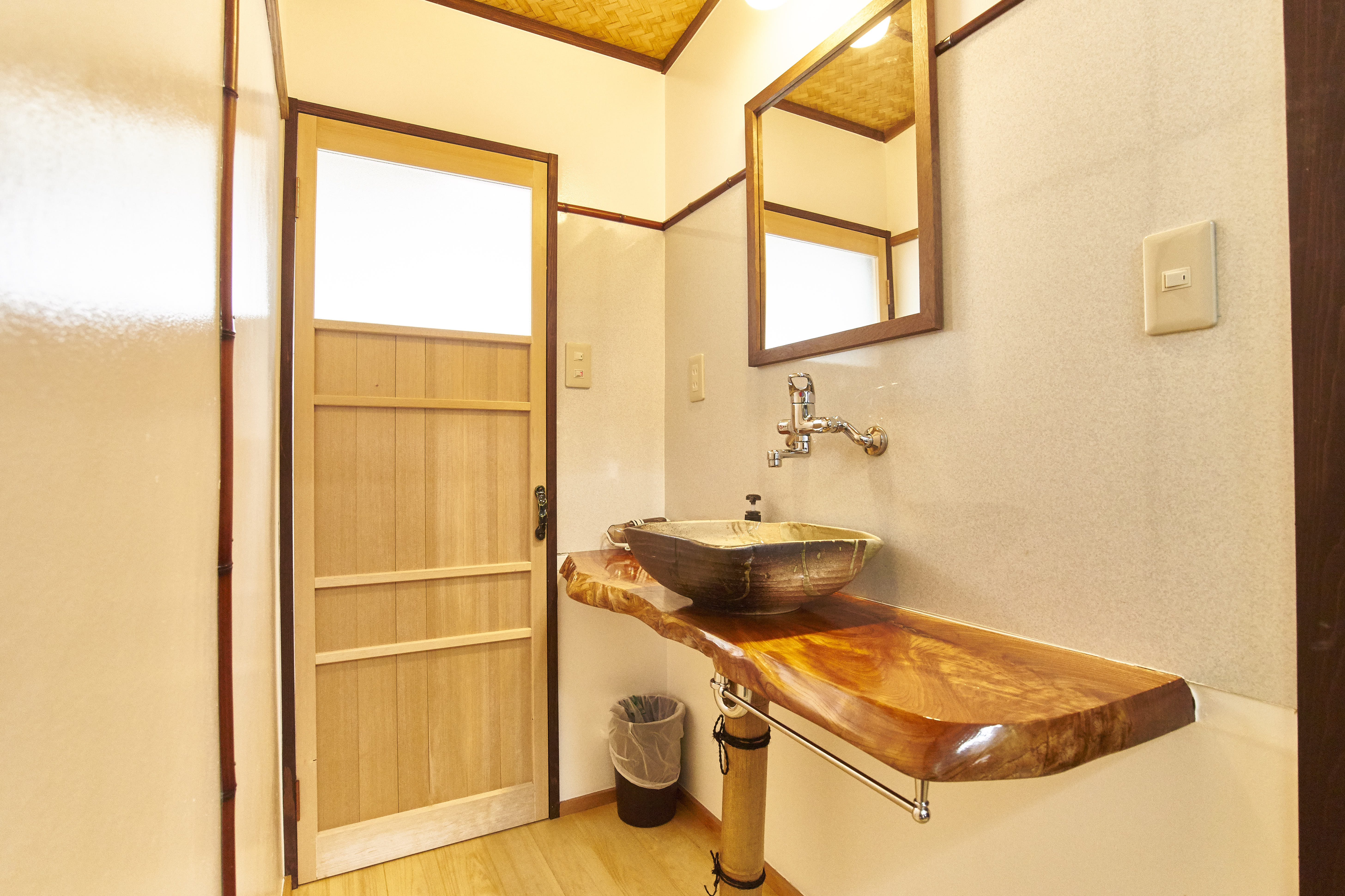 Artisan powder room with live-edge wooden counter, ceramic vessel basin, woven bamboo ceiling, and natural light