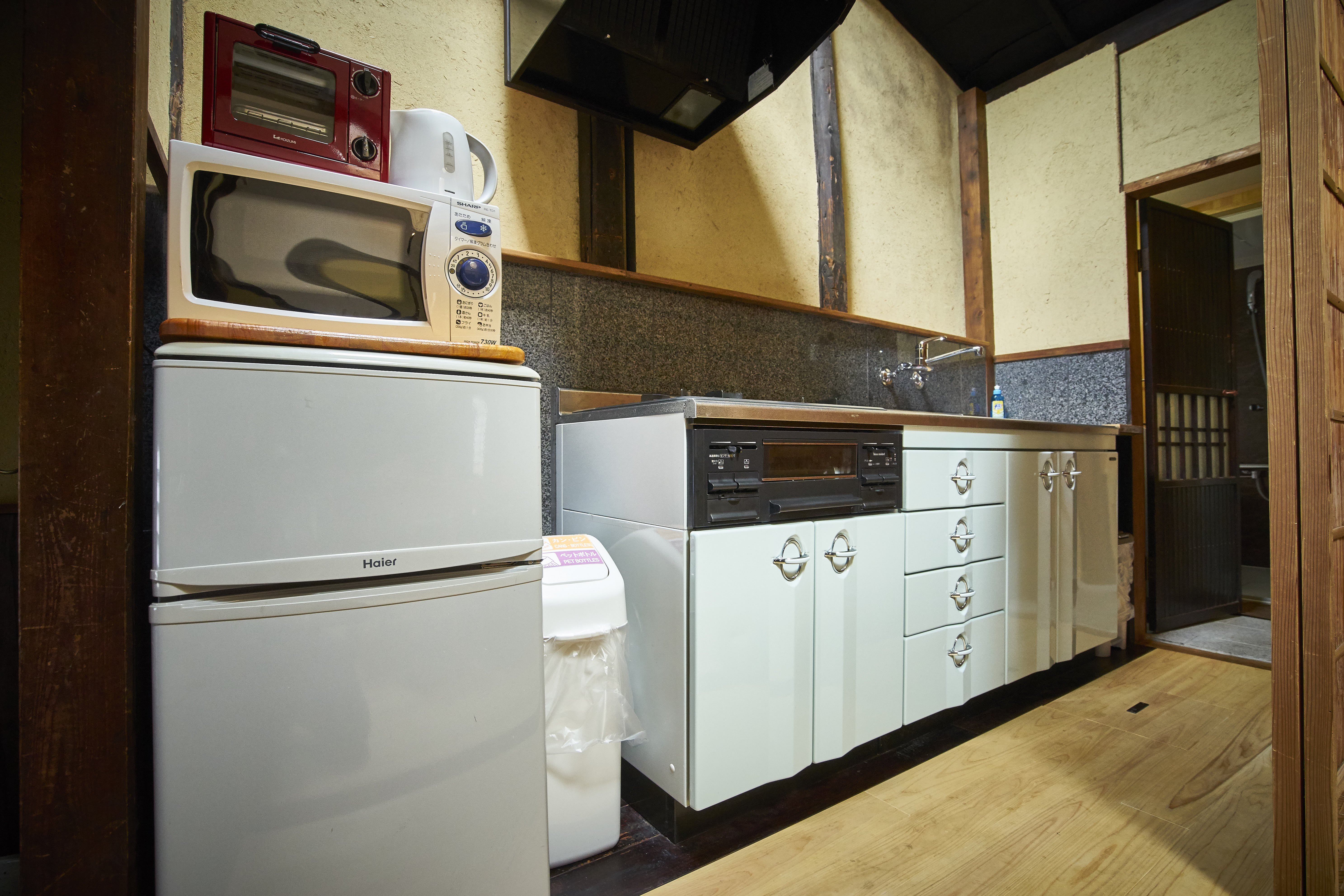 Rustic machiya kitchen with exposed beams, fridge, microwave, toaster oven, and traditional white cabinet drawers