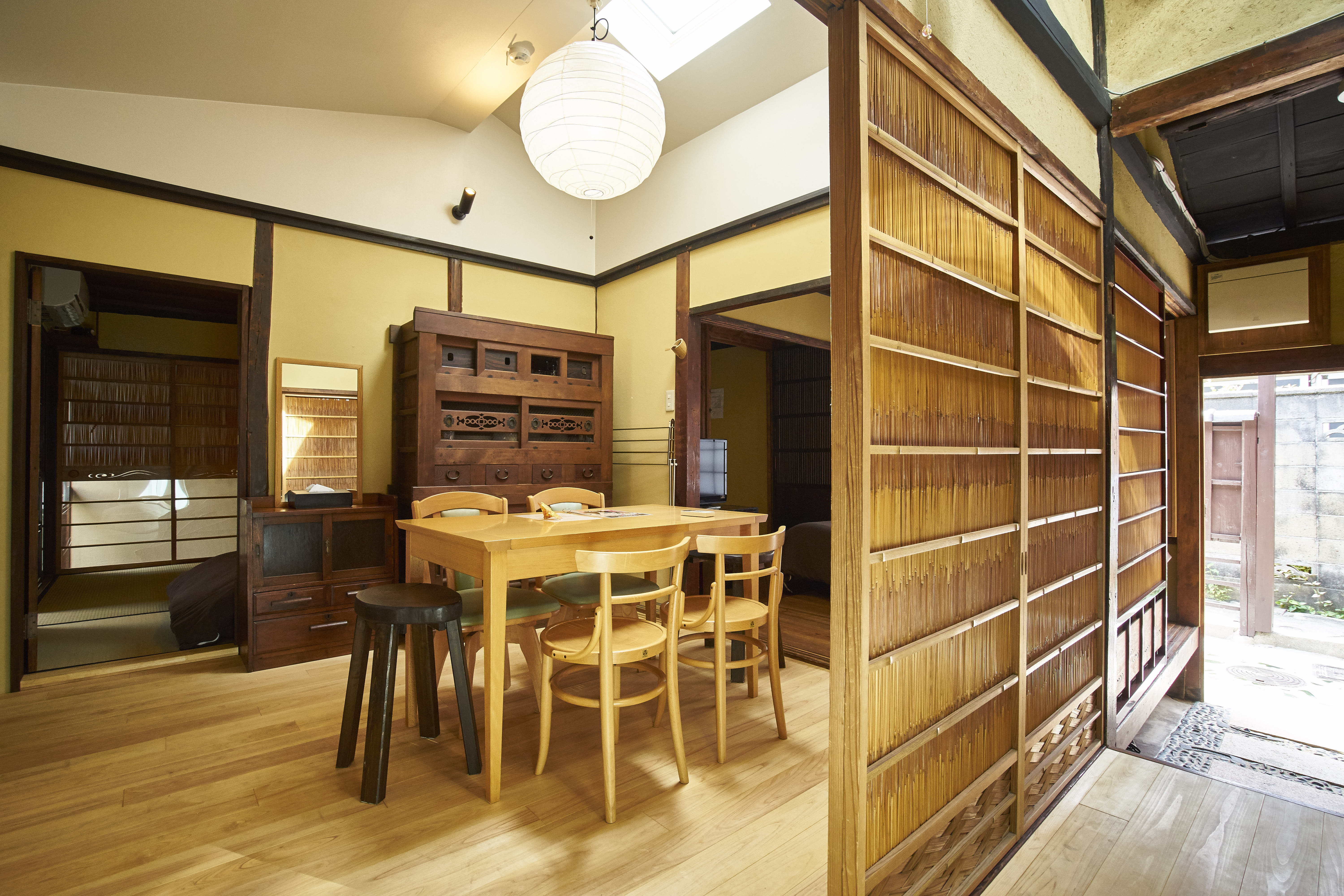 Spacious traditional living and dining area with high ceilings, paper lantern, wooden dining table, antique tansu, and bamboo screen walls