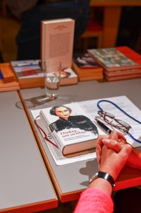 Buch „Denken um zu leben“ liegt auf einem Tisch, daneben gefaltete Hände