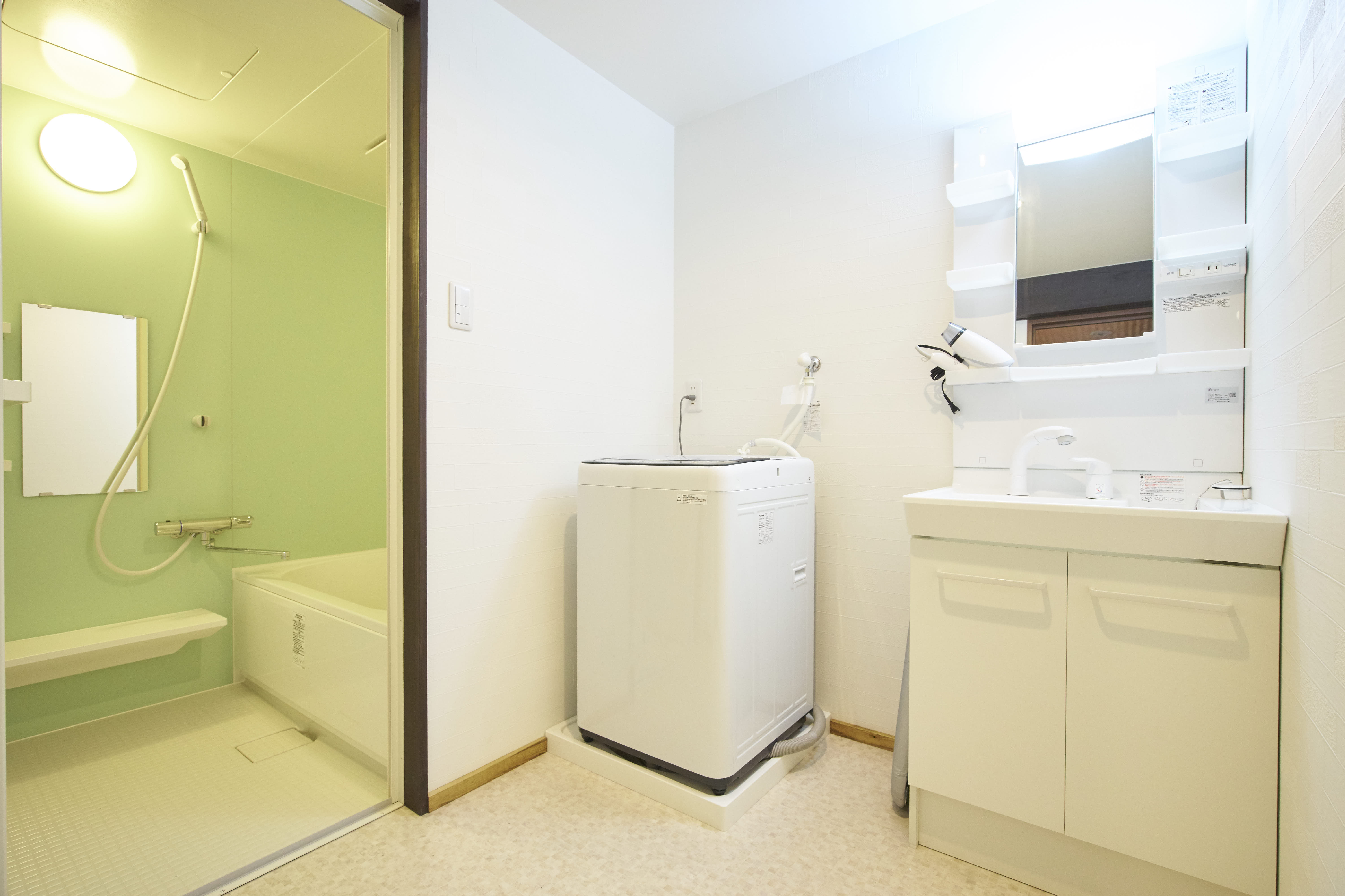 Bright bathroom with green-tiled shower room, soaking tub, washing machine, and vanity unit