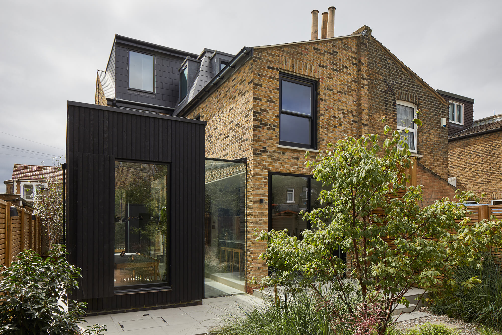 Modern extension with black timber cladding and floor-to-ceiling glazing against traditional London stock brick facade