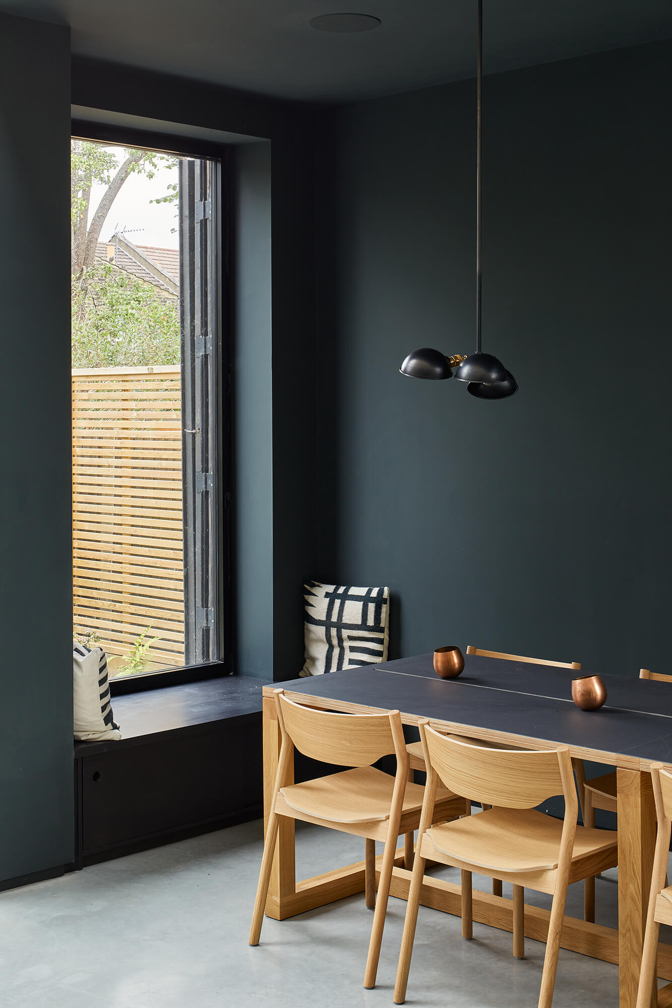 Dining area with dark green walls, wooden chairs, and built-in window seat overlooking garden