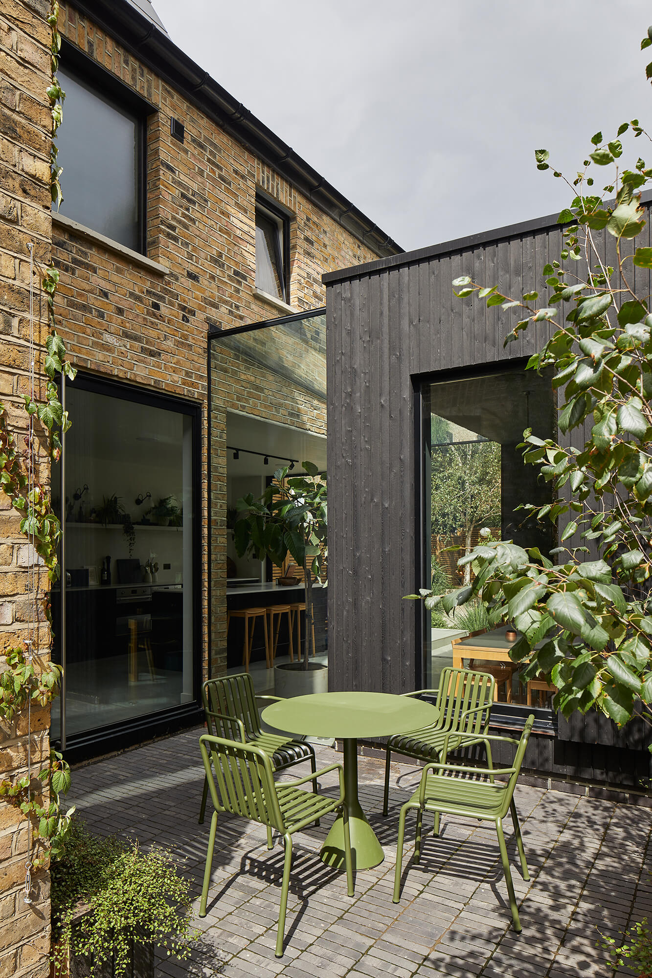 Outdoor terrace with green metal furniture set against black timber cladding and brick walls