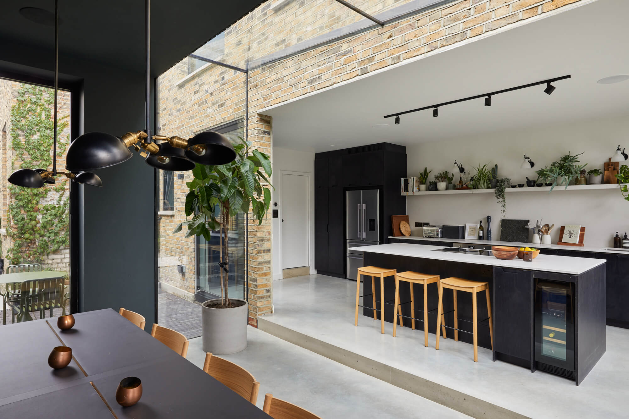 Contemporary kitchen with black cabinets, white countertops, and wooden bar stools under track lighting