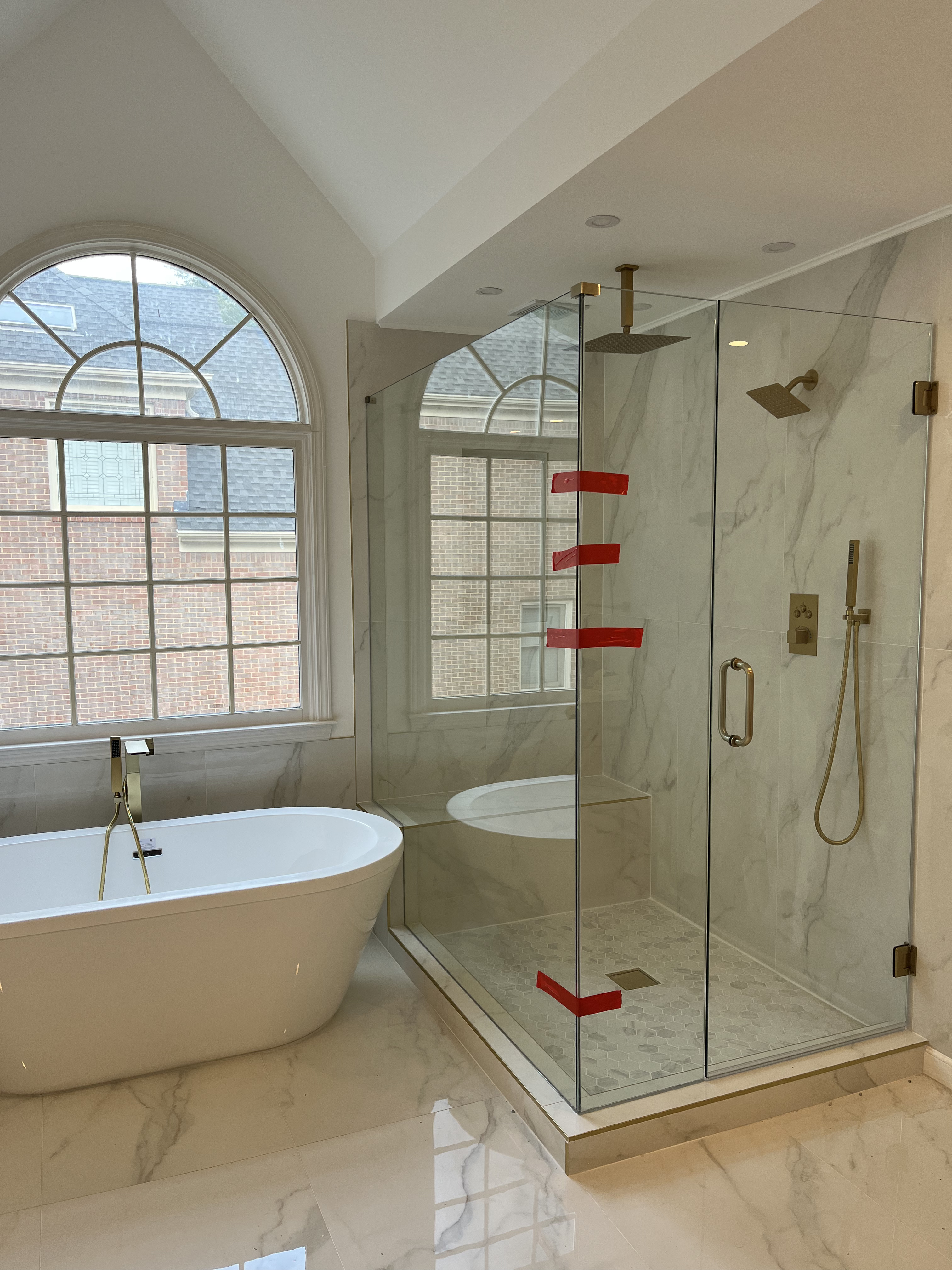 Contemporary spa bathroom with freestanding white tub, marble walls with gold veining, frameless glass shower, integrated shelving