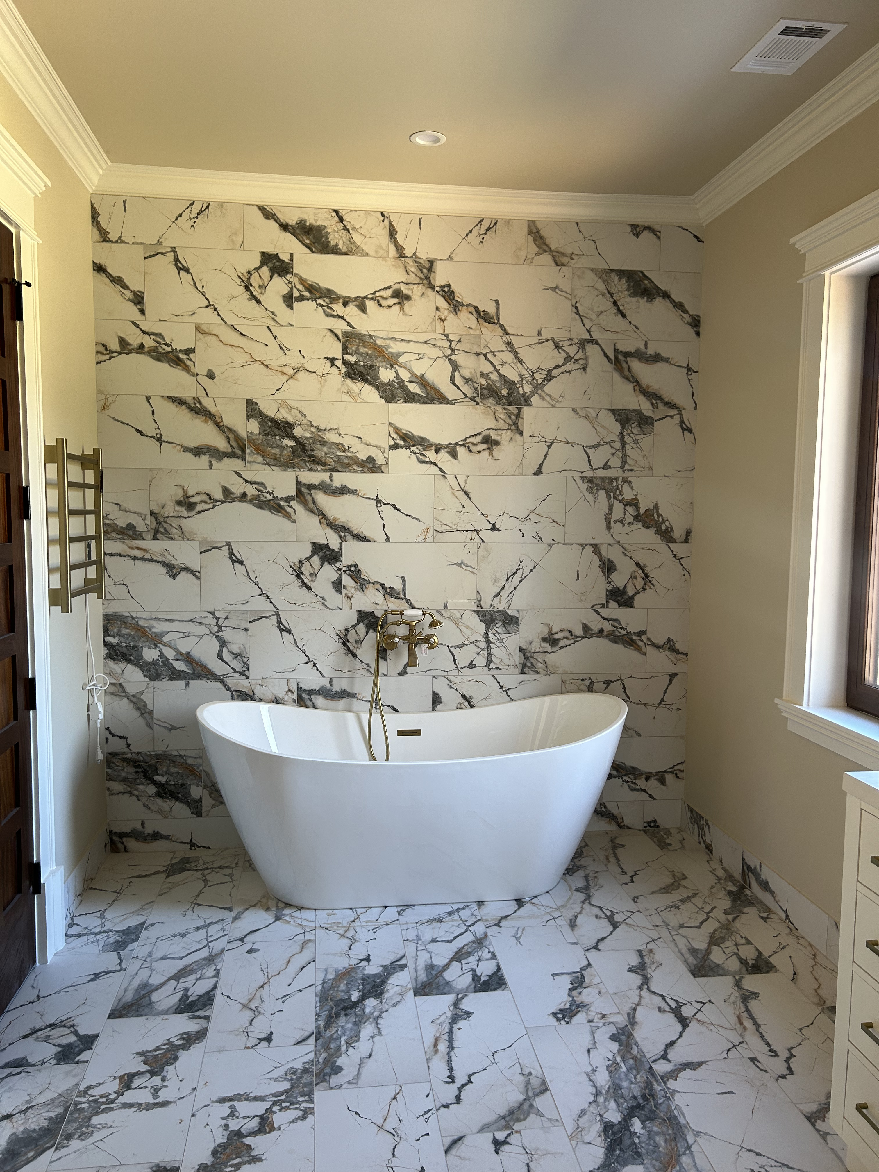 Elegant marble bathroom with white freestanding tub, large-format marble tile wall and floor, natural light, brass fixtures