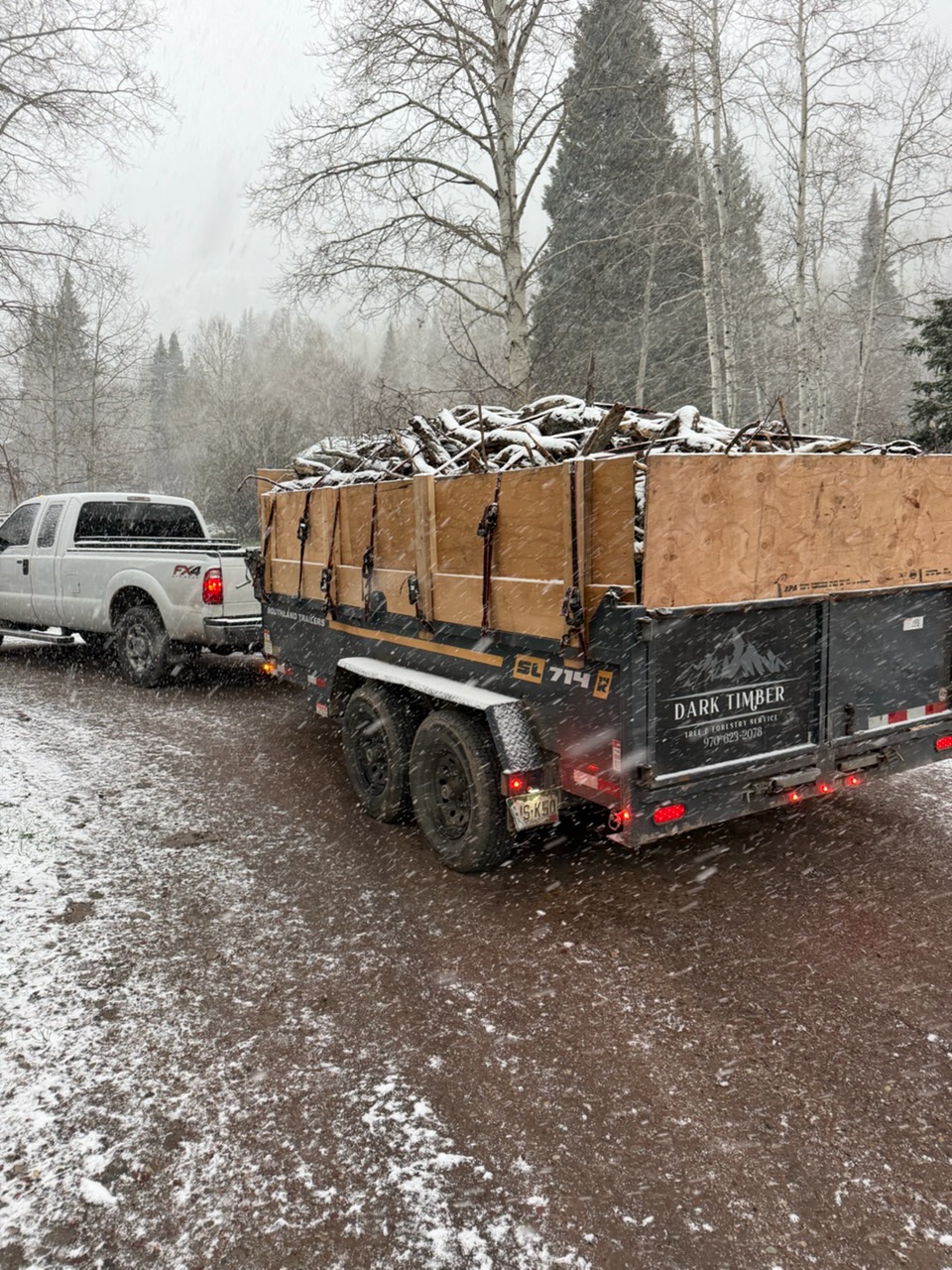 Dark Timber truck and branded trailer loaded with debris in falling snow