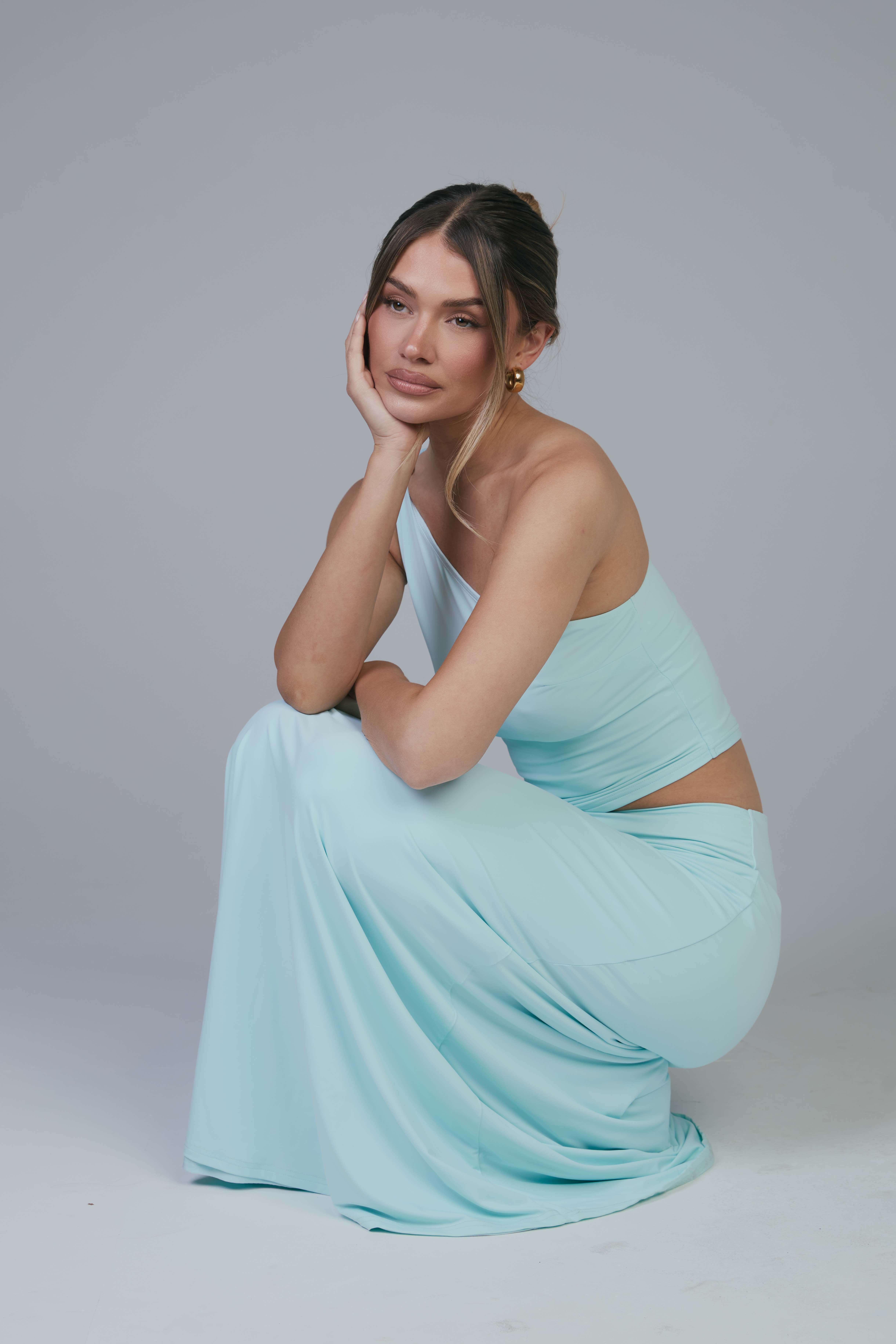 Mollie crouching in aqua set with chin resting on hand, gazing away