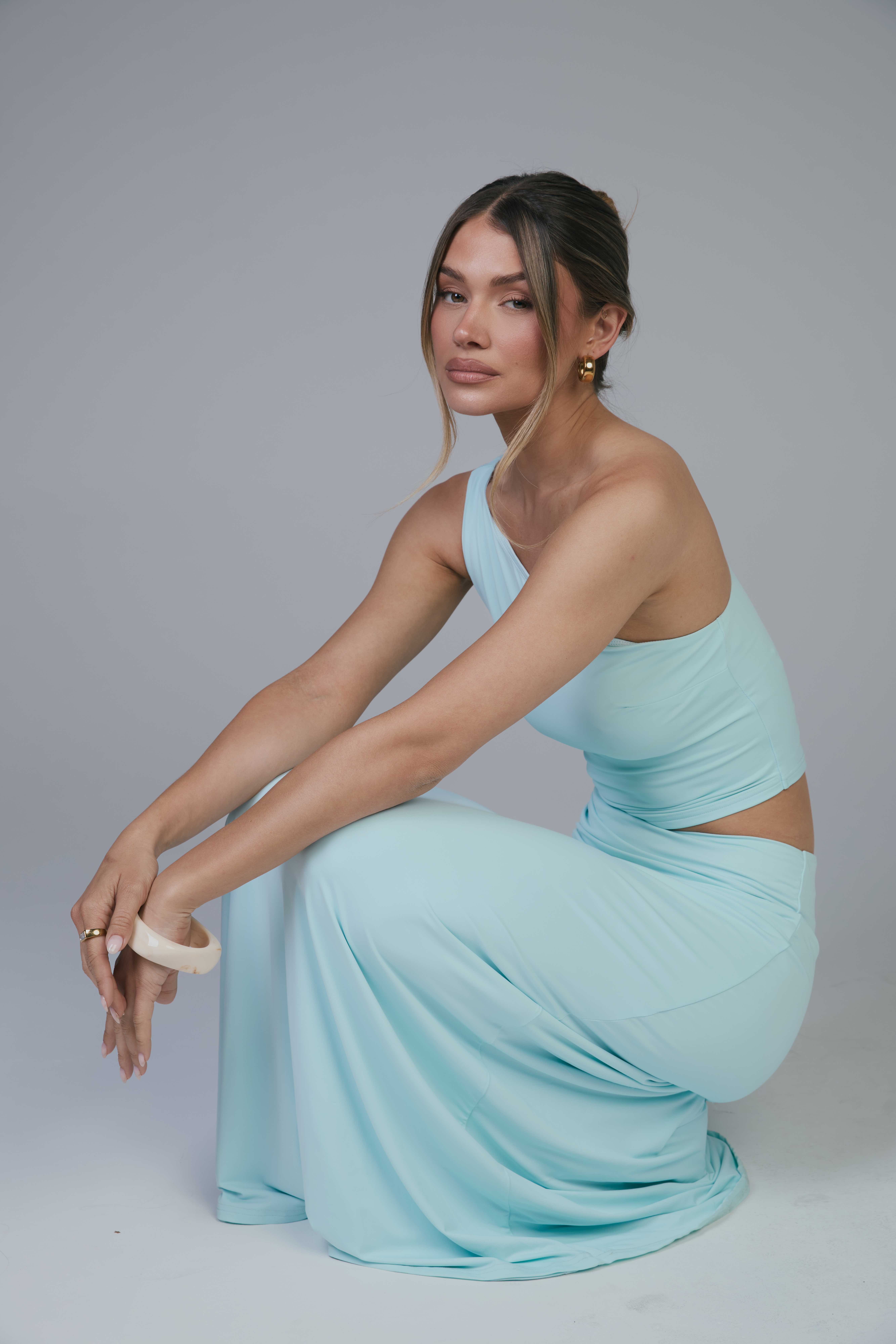 Mollie crouching side profile in aqua set, arms over knees, looking at camera