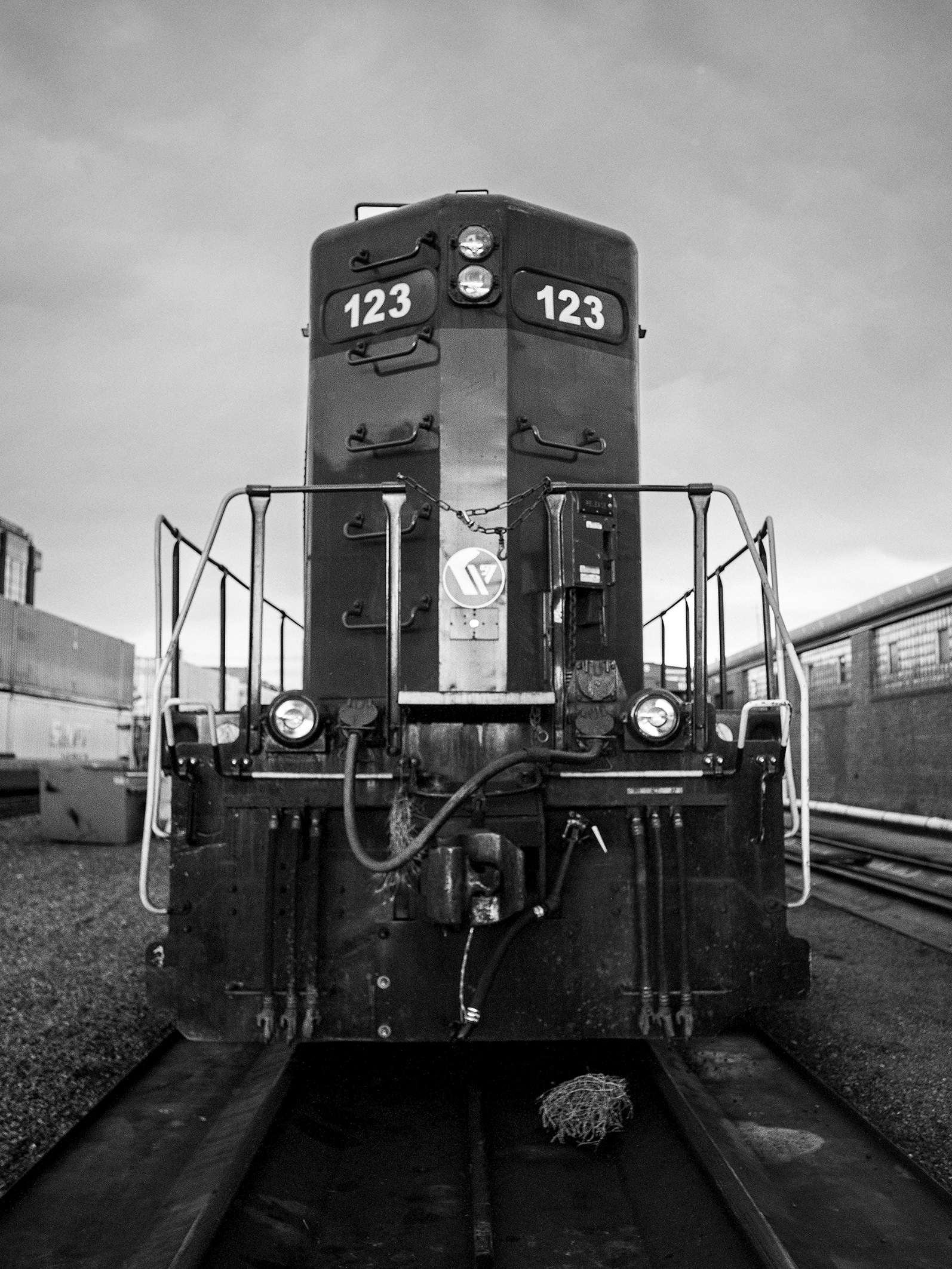 Front view of diesel locomotive engine number 123 in rail yard with industrial backdrop