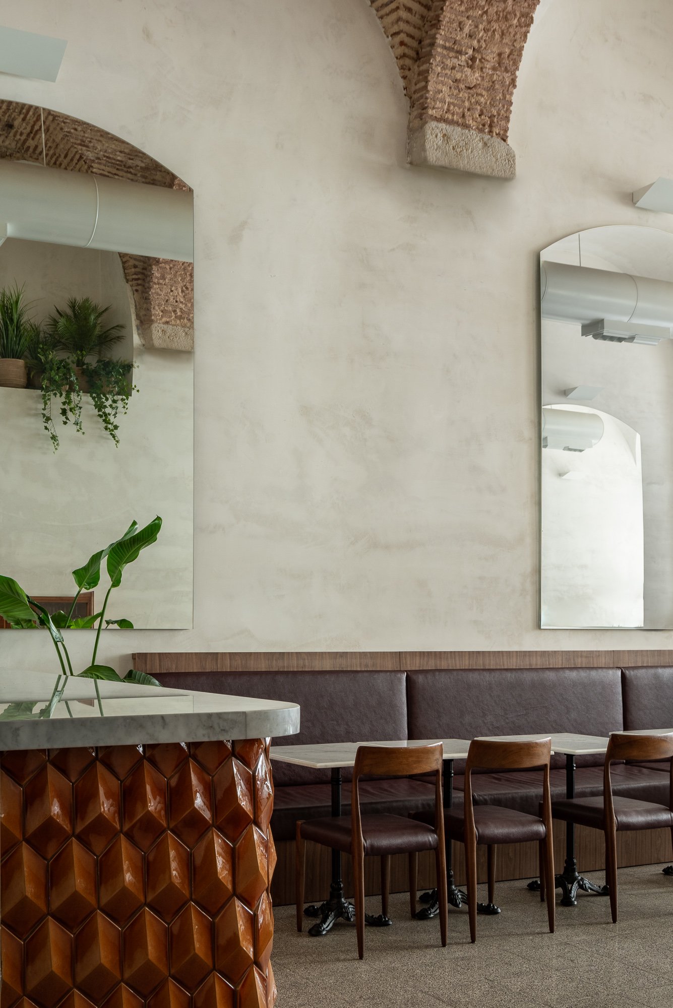 Detail of dining area with sculptural textured table base and mirrors reflecting exposed brick arches