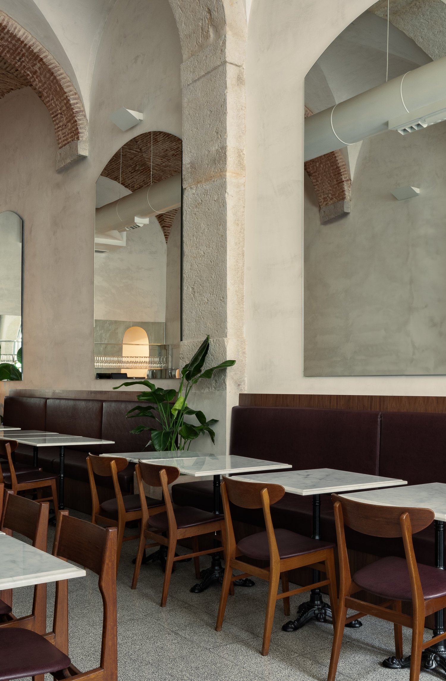 Dining area with mid-century modern wooden chairs and marble tables against stone columns and plastered walls