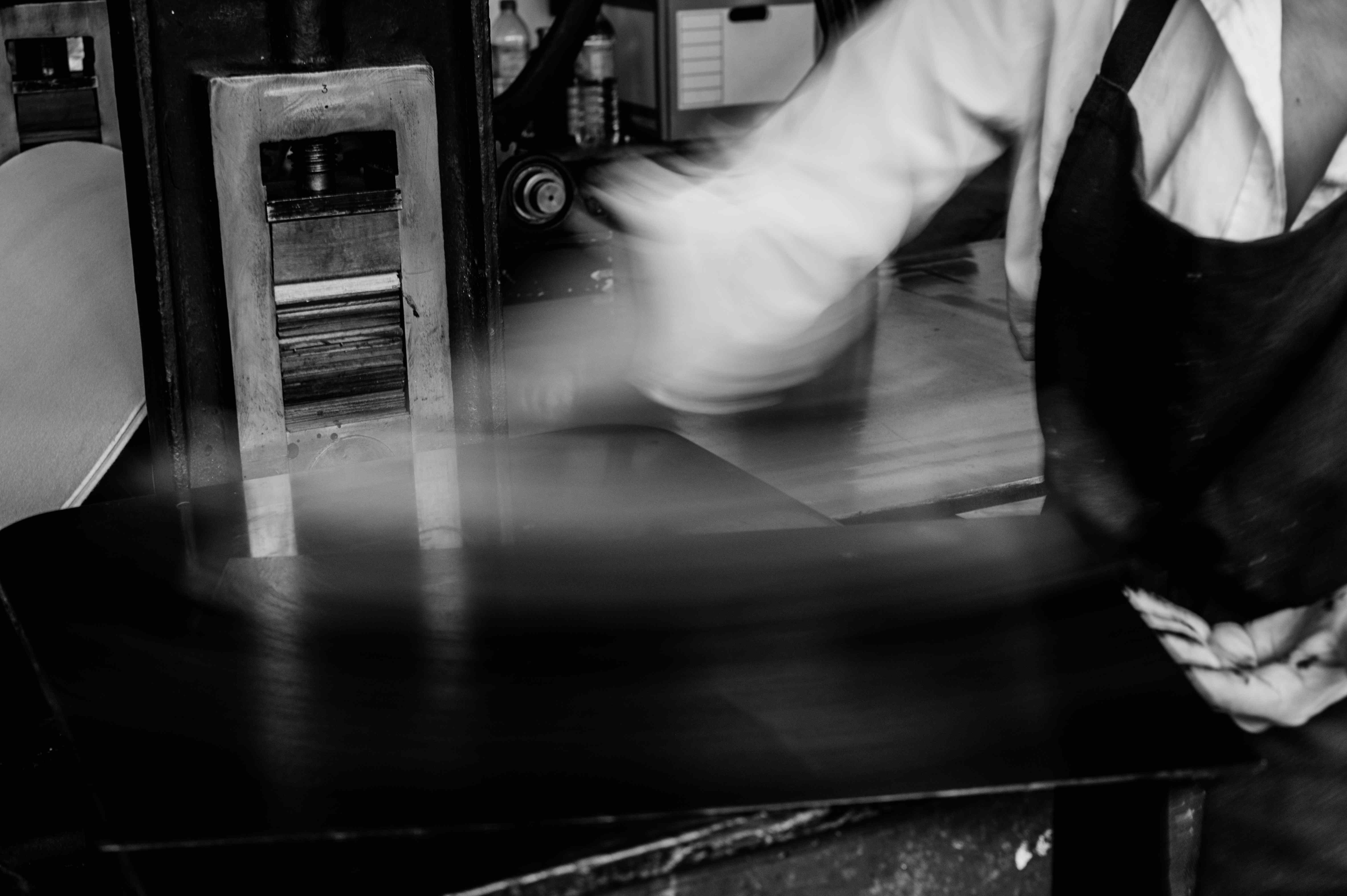 Hands moving across the bed of an etching press.