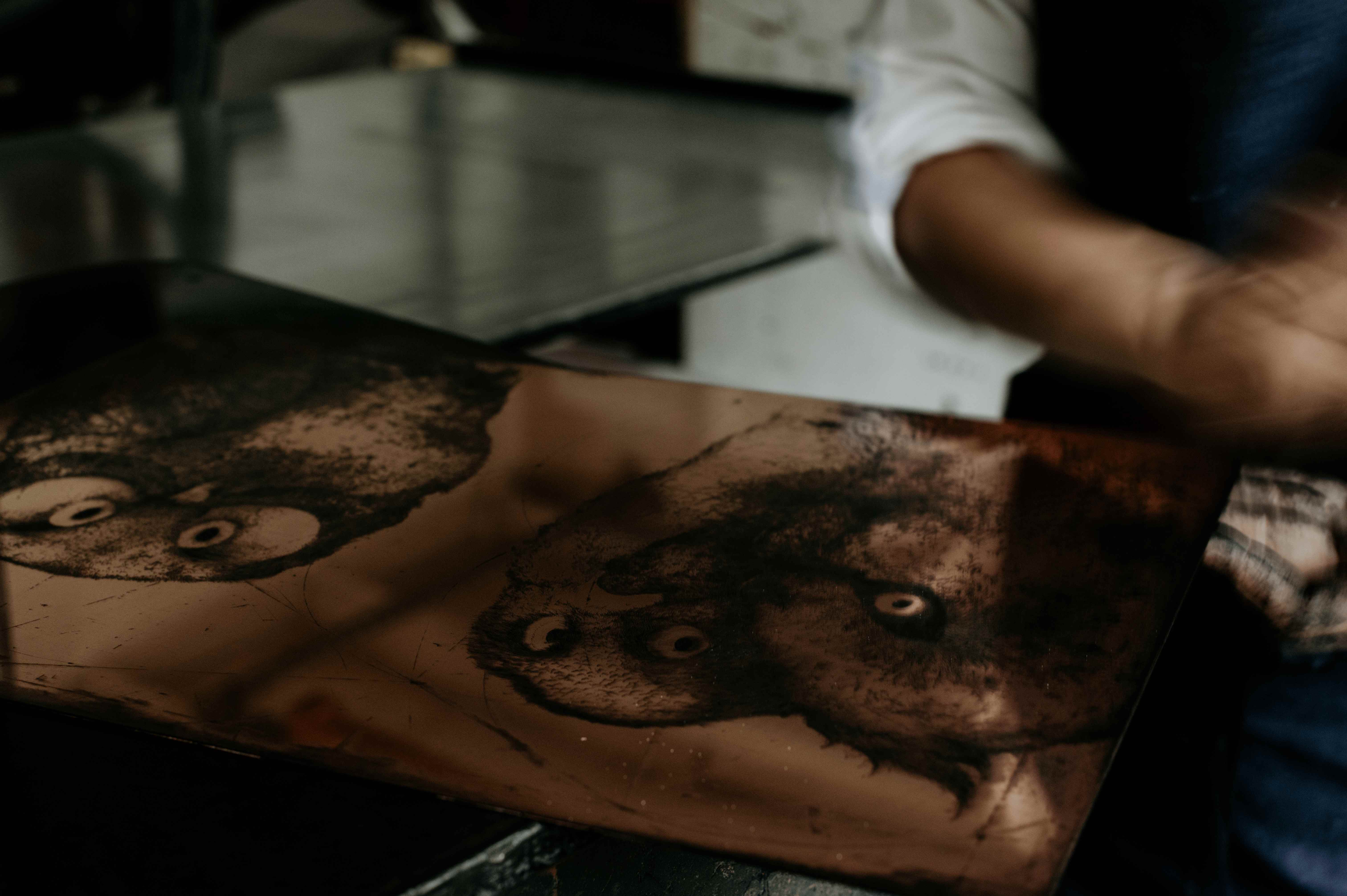 Inked copper plate with owl portraits on the press bed.