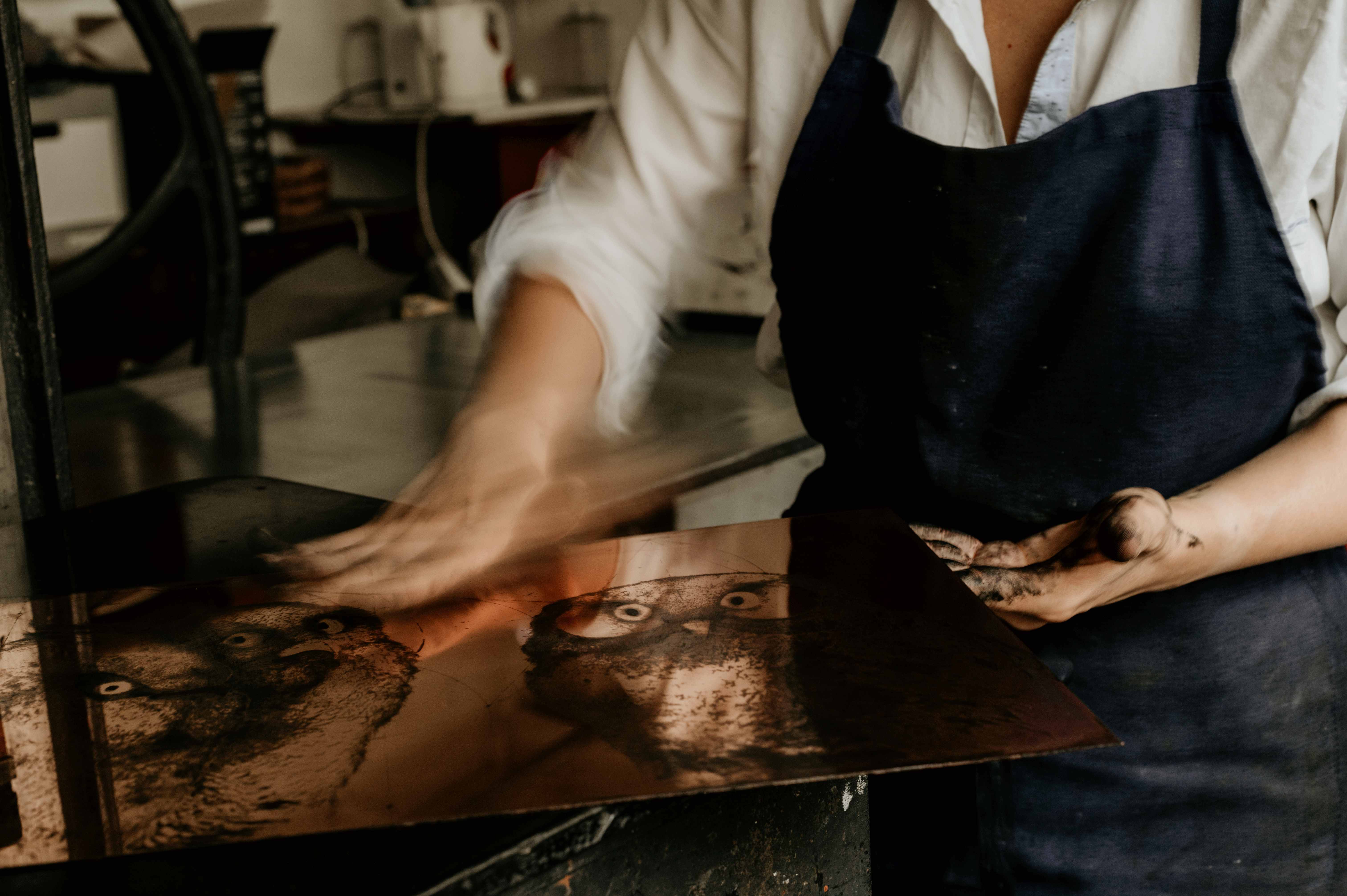 Wiping an inked copper plate showing two owls before printing.