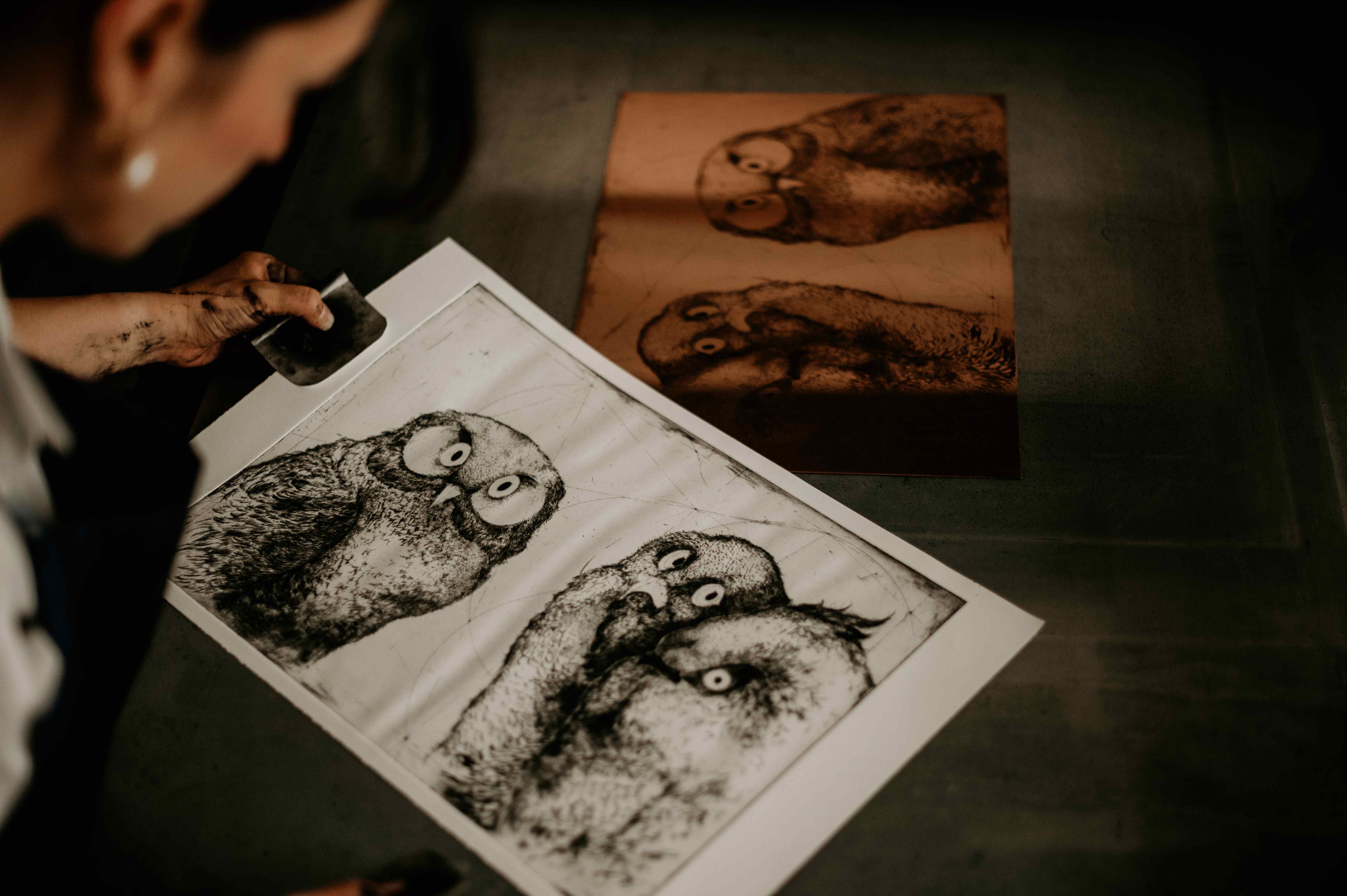 A finished owl print being lifted beside the etched copper plate.