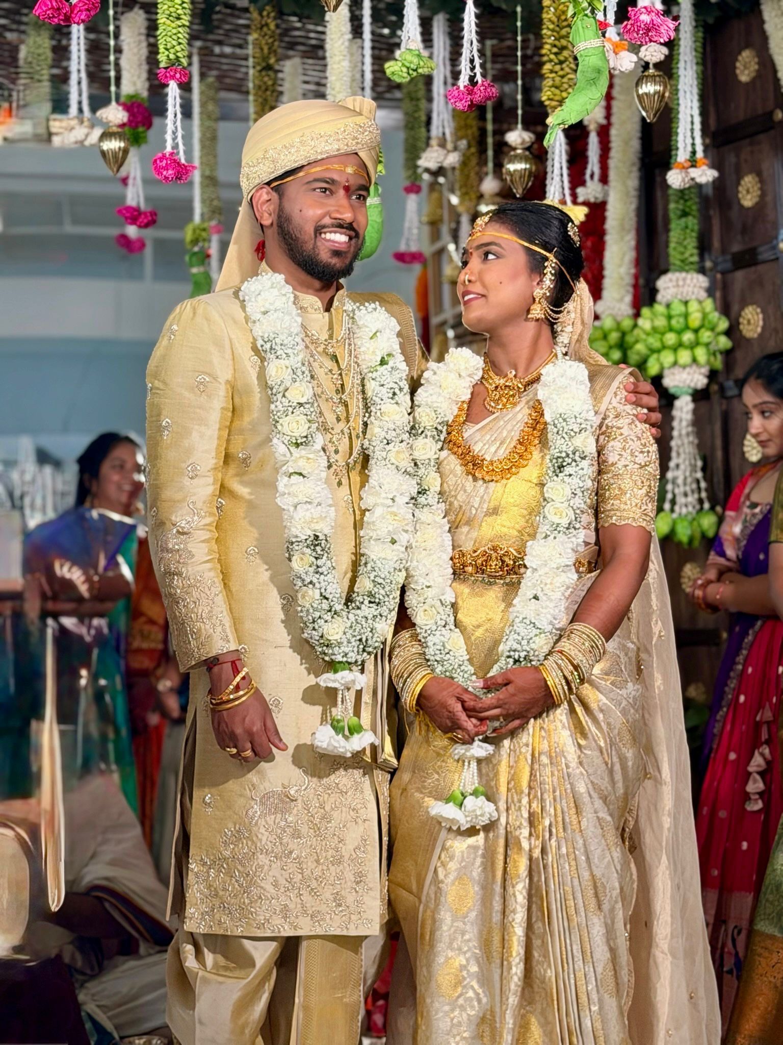 South Indian wedding couple in traditional gold attire with white flower garlands under a floral mandap