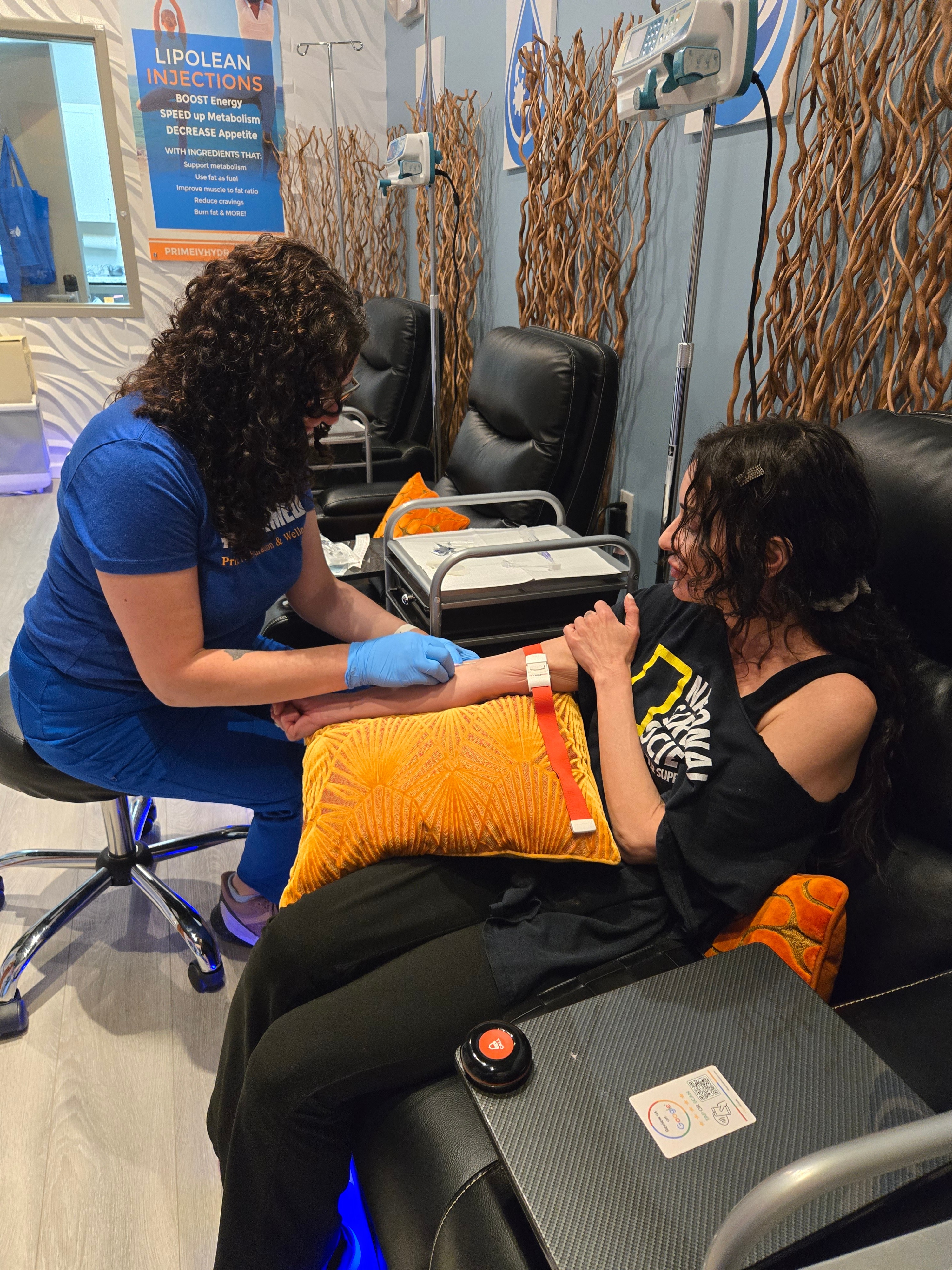 A Prime IV nurse placing an IV in a smiling client's arm beneath a LipoLean Injections poster