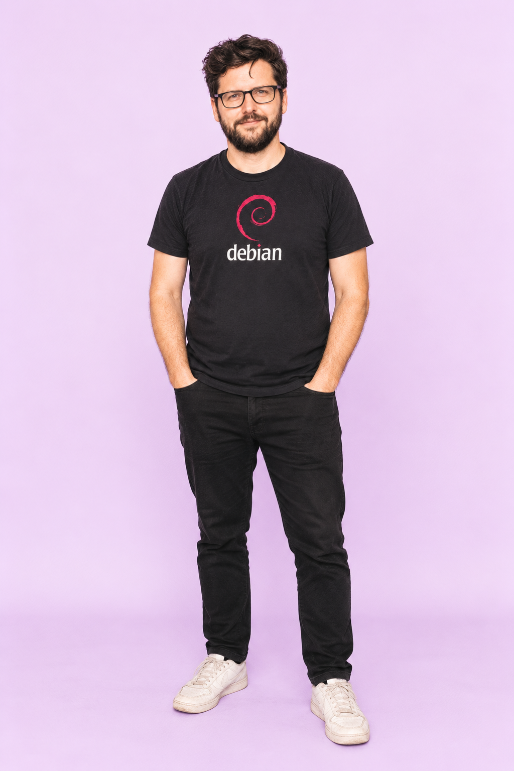 Michael Kendy wearing glasses and a black Debian T-shirt against a lavender background