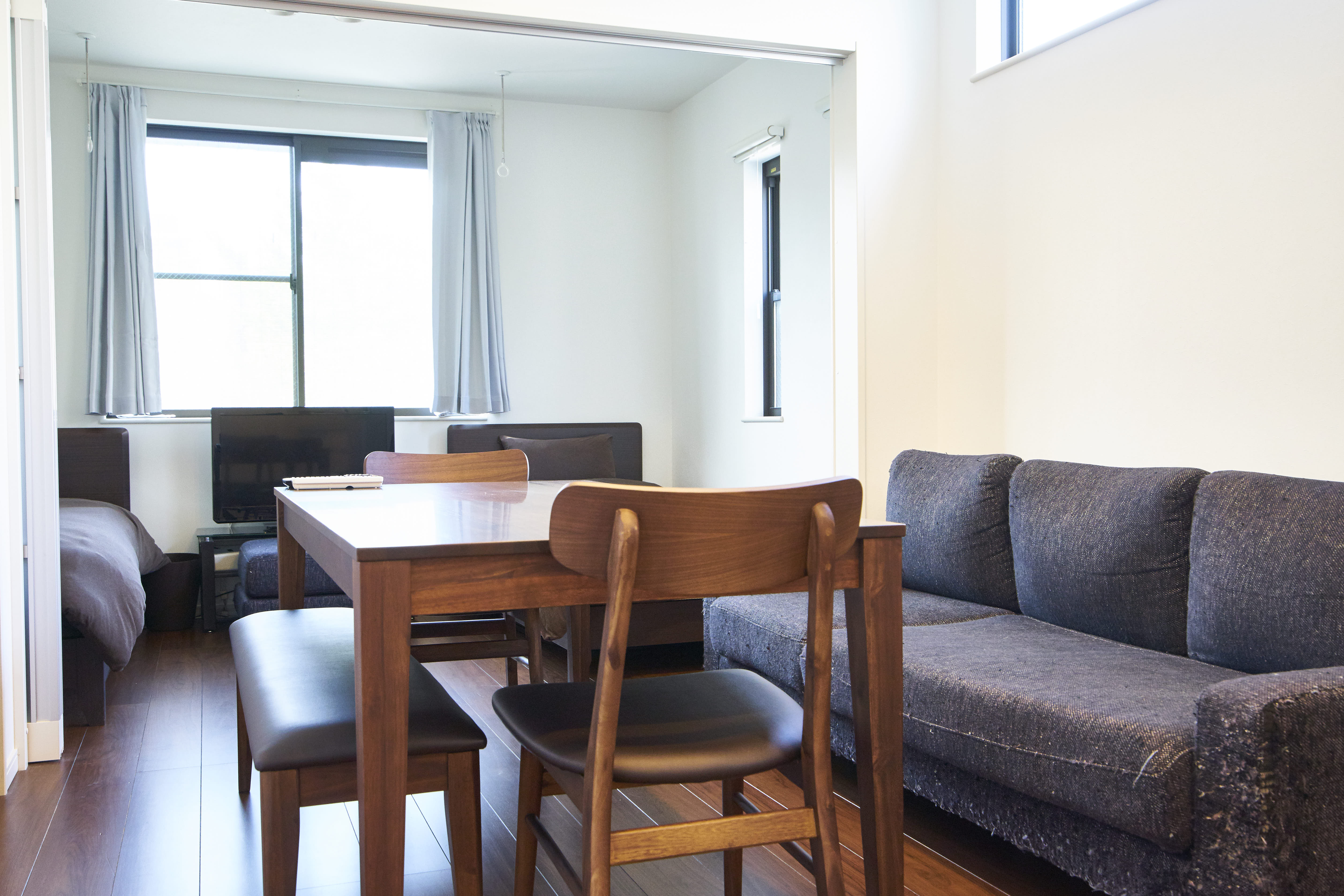 Bright 2F living space with wooden dining table, chairs, grey sofa, and natural light