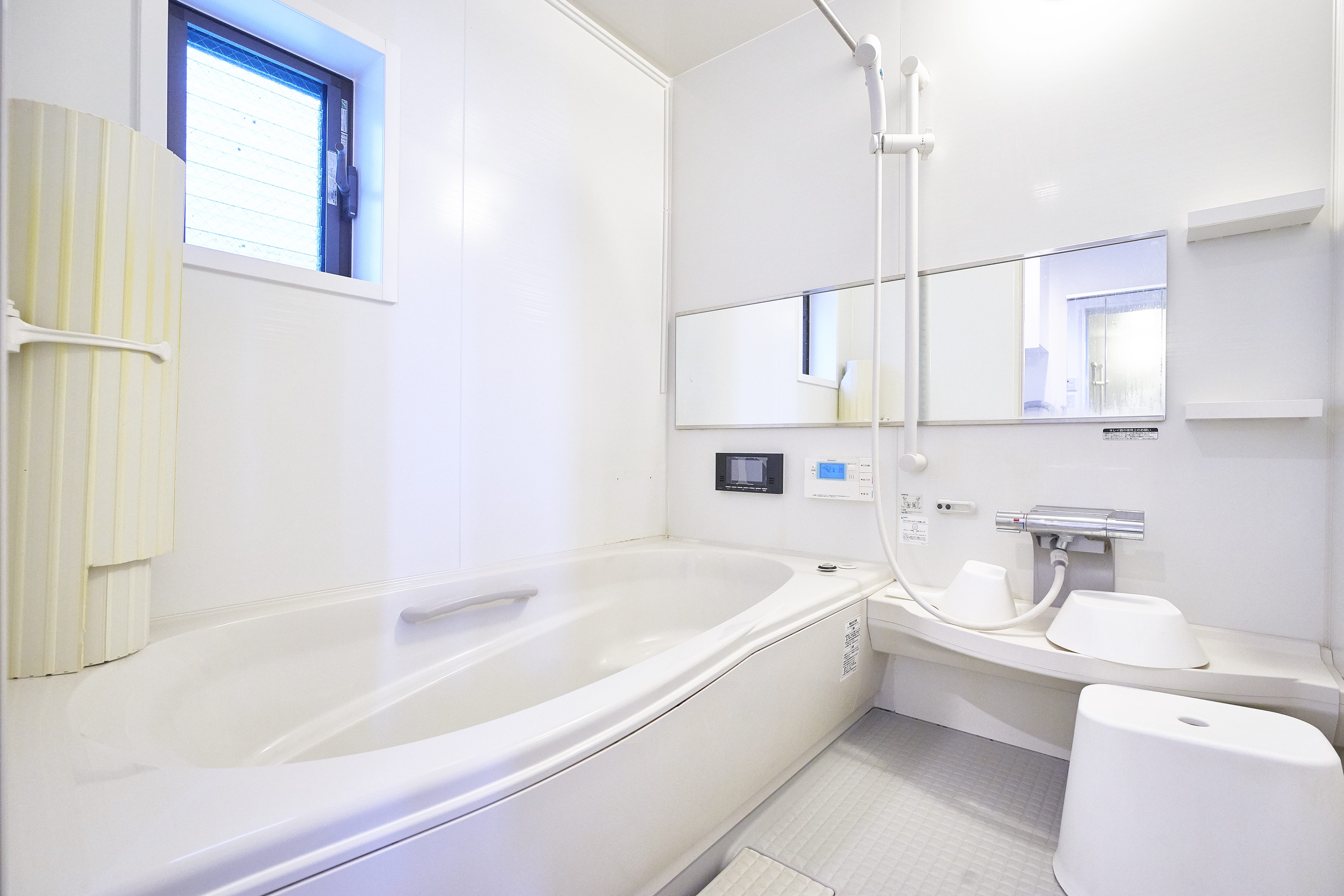 Spacious Japanese bathroom with large white soaking tub, built-in TV, and shower area