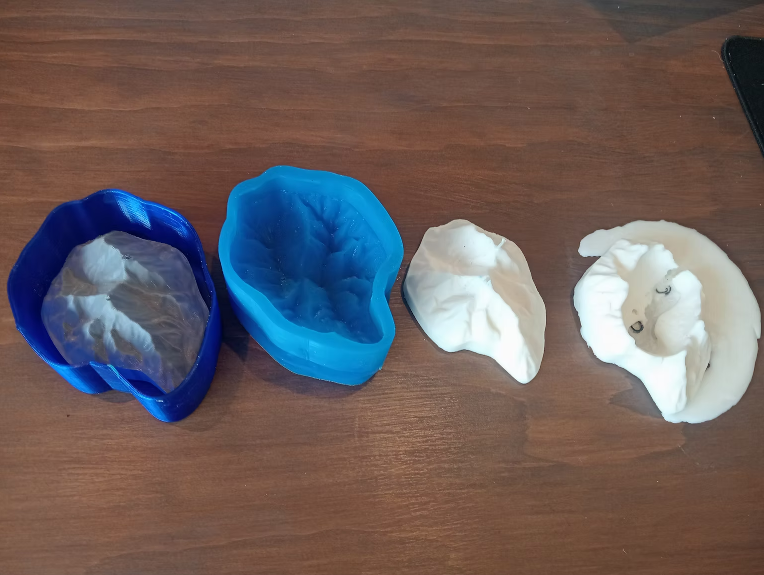 Blue 3D printed mould shells and white silicone mountain-shaped candle casts laid out on a wooden table